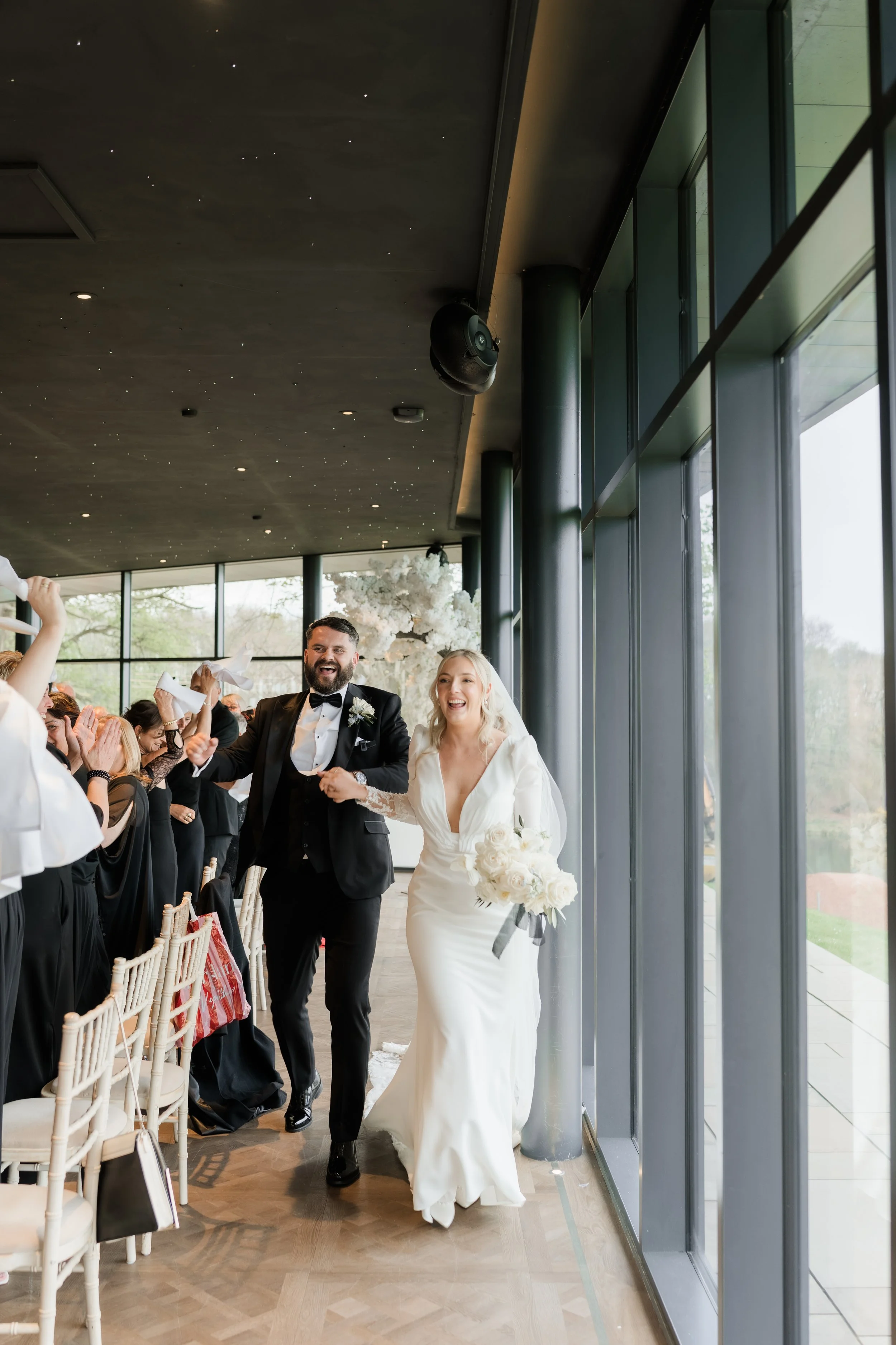 A bride and groom walking down the aisle happily after their wedding ceremony, with guests clapping and celebrating.