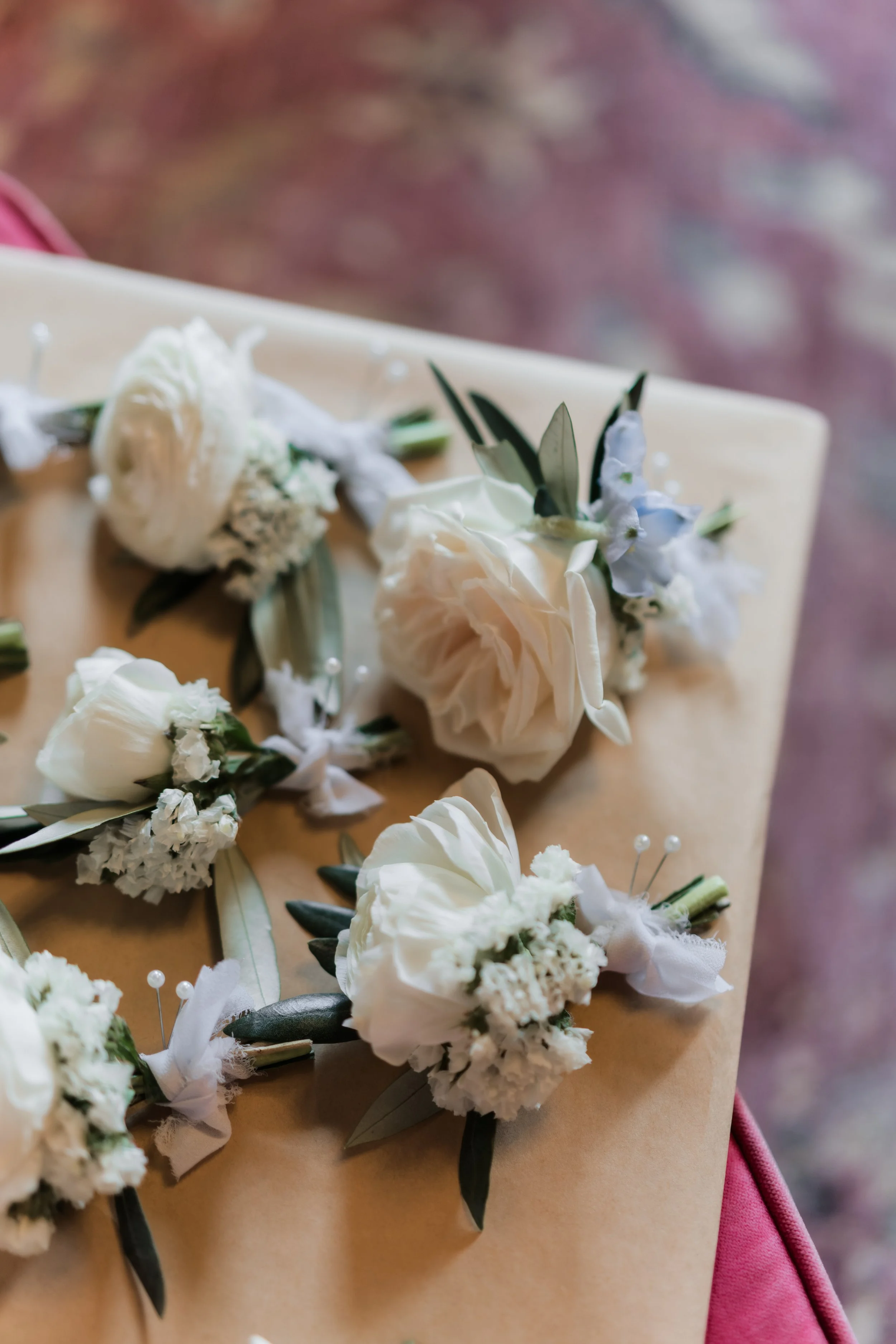 Various white flowers, including roses, placed on a light-colored surface with a blurred reddish background.