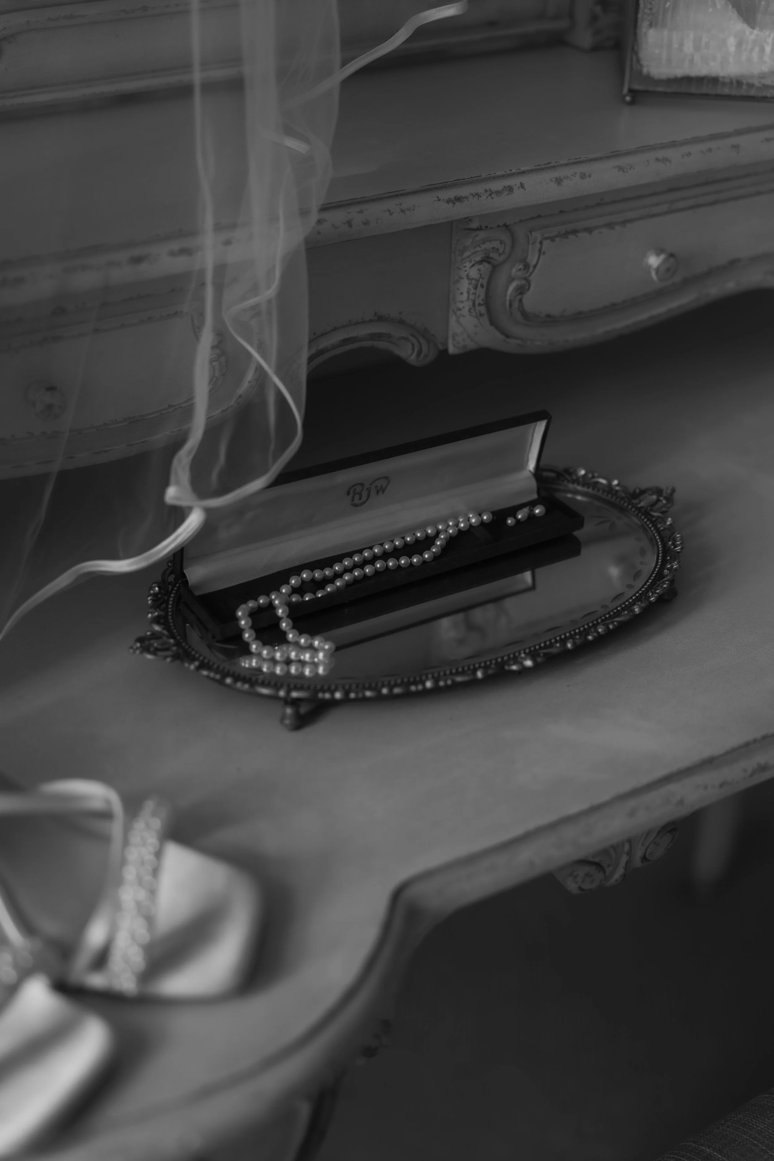 A pearl necklace in an ornate jewelry box on a vintage vanity table with a mirror.