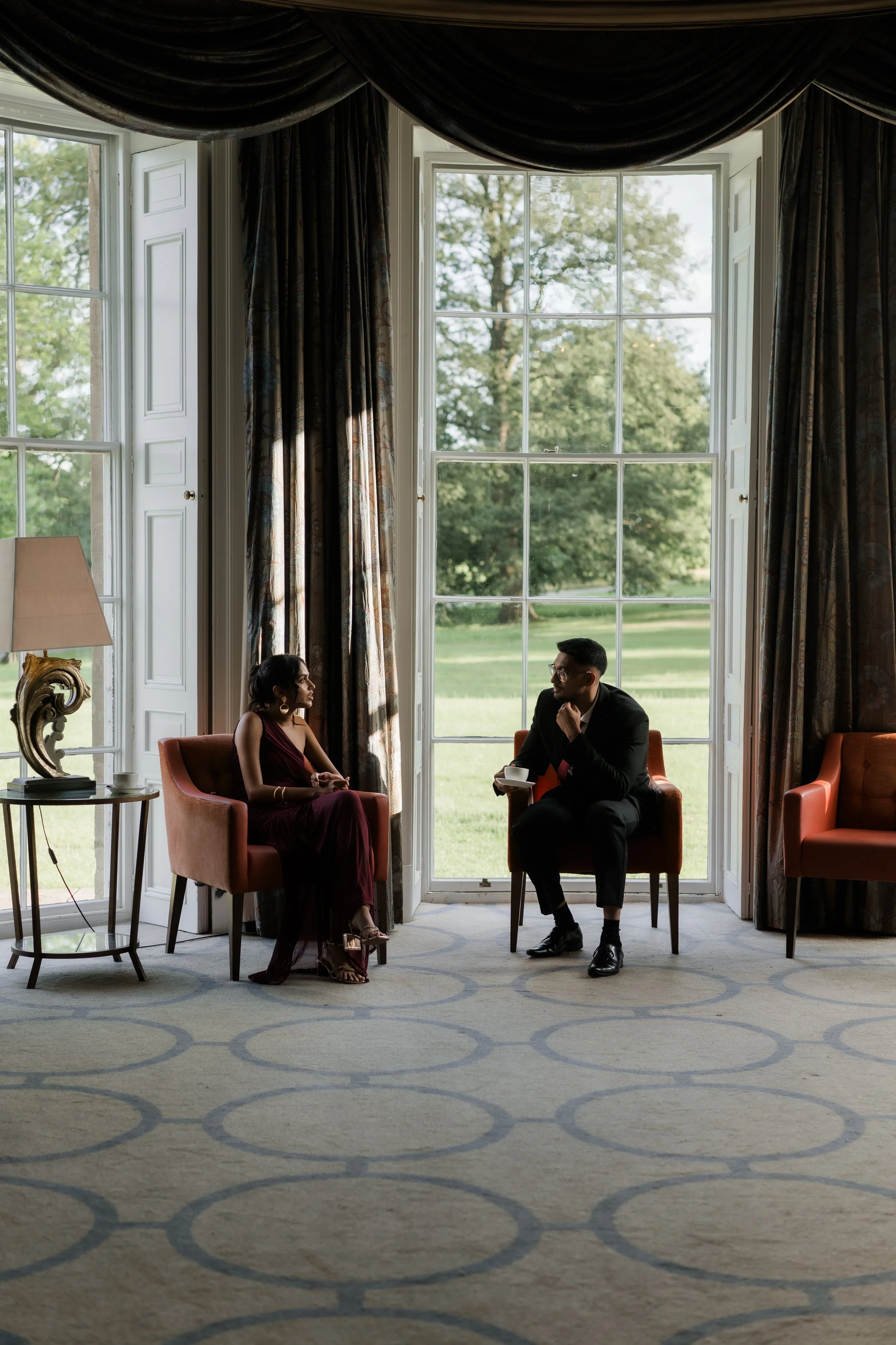 Wedding guests sit in large window talking and drinking tea. Ruddnig park. North Yorkshire