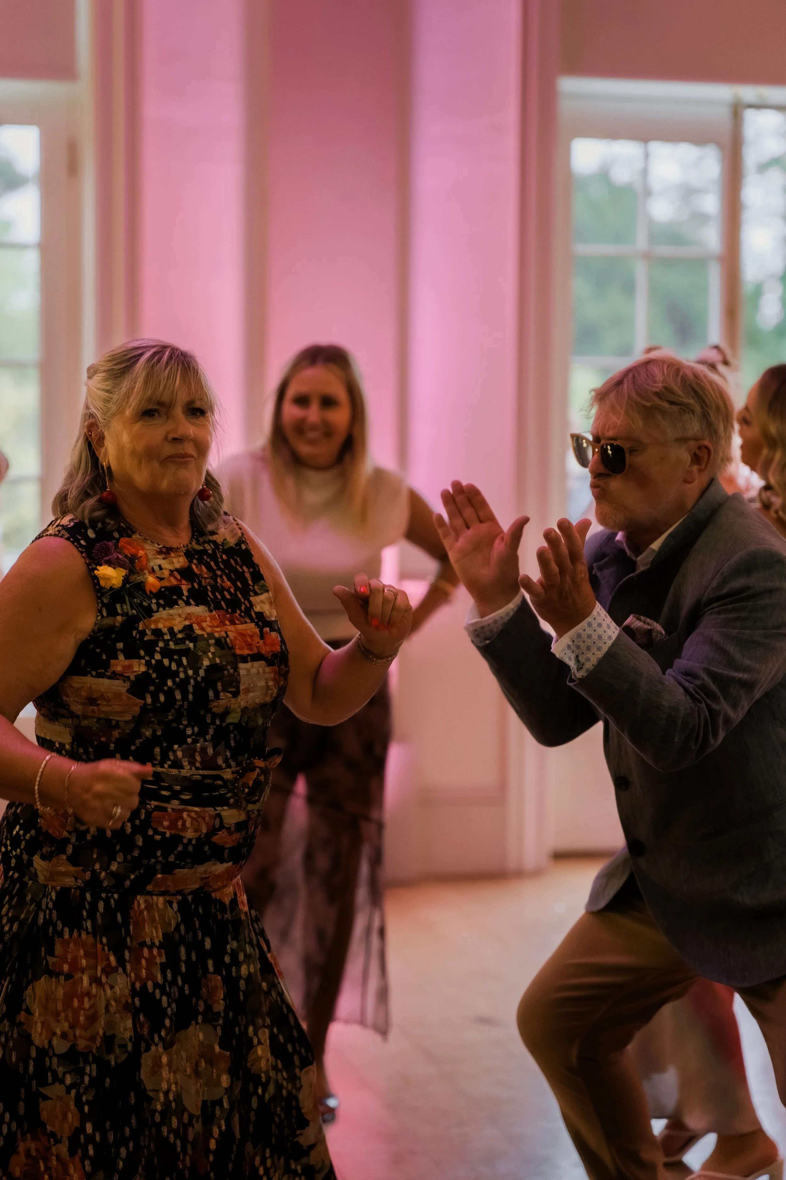 People dancing at a social event in a room with pink walls, lively atmosphere.