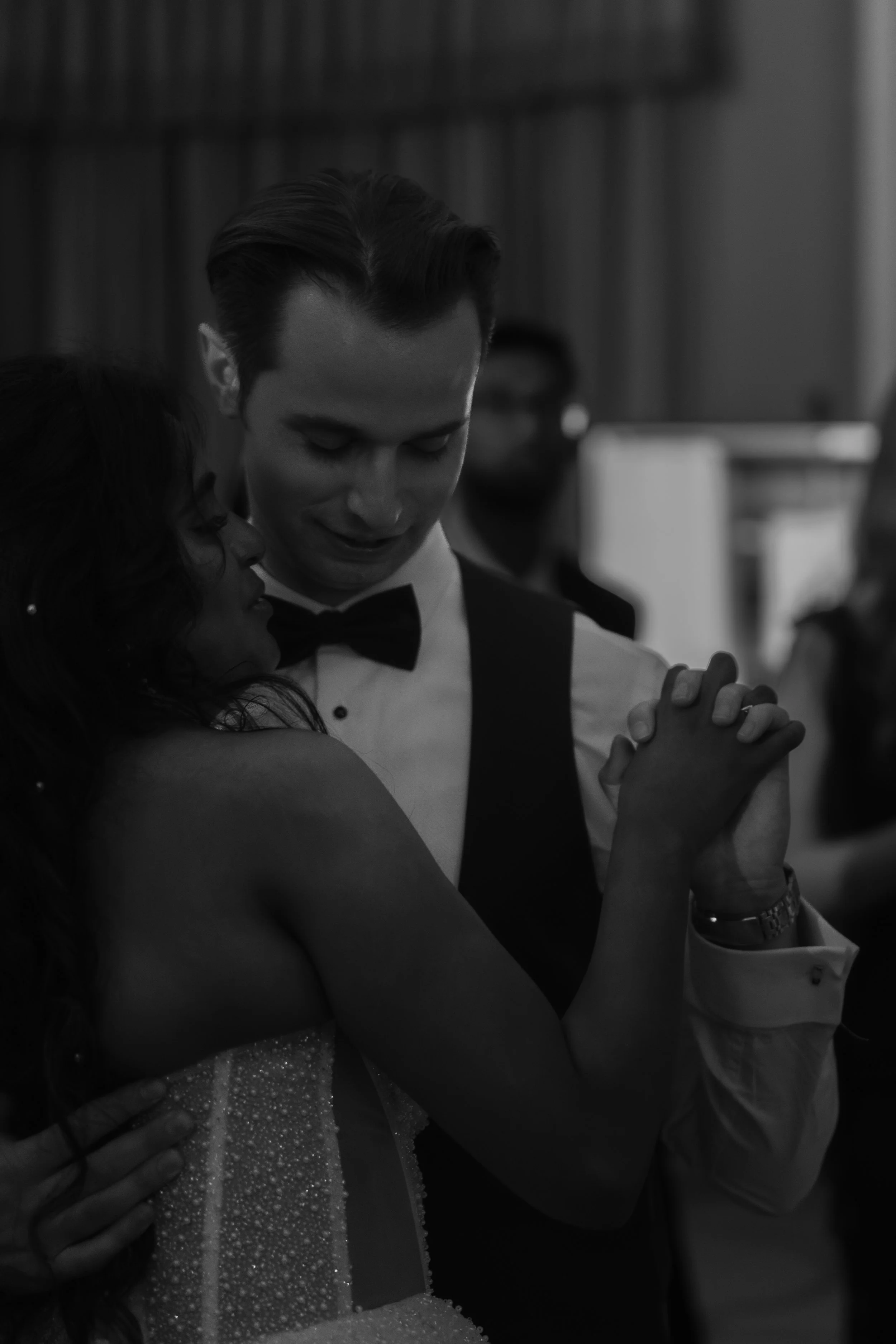 A black-and-white photograph of a couple dancing closely, the man in a tuxedo and the woman in a strapless dress, holding hands and looking at each other affectionately.