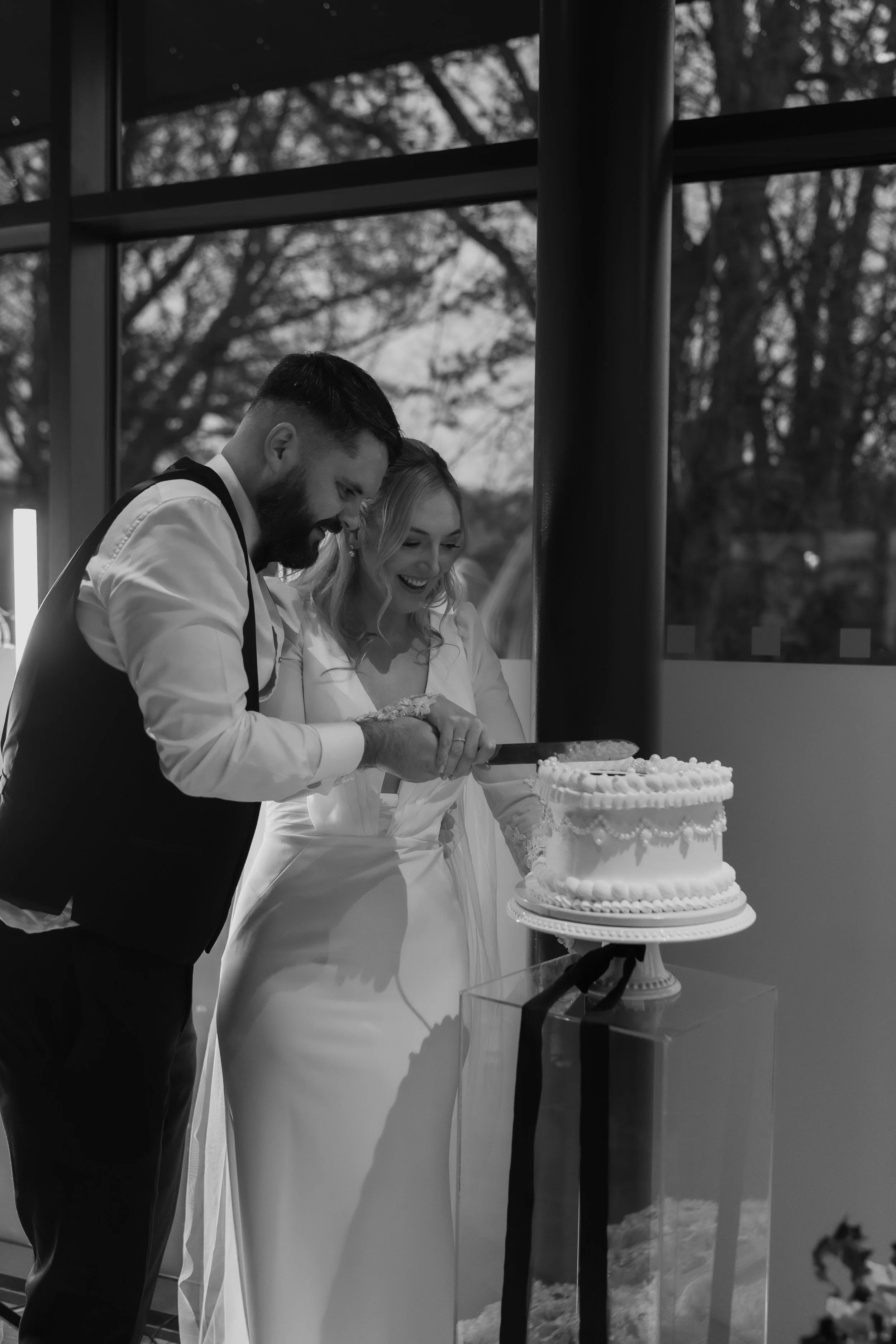 A couple, a bride and groom, cutting a wedding cake together at their wedding reception.