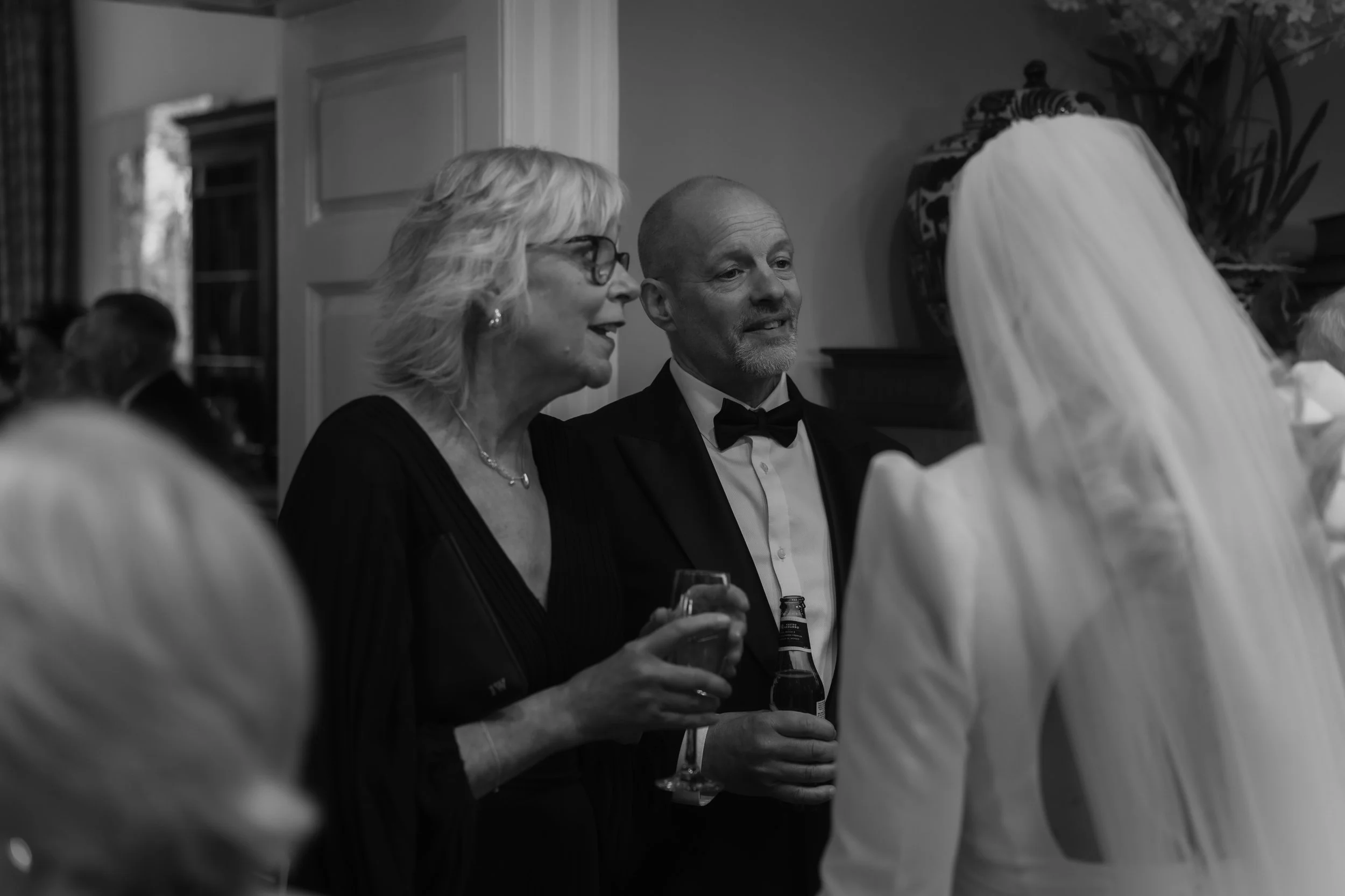 A woman and a man in formal attire talking to a bride in a wedding dress at a celebration or wedding reception.
