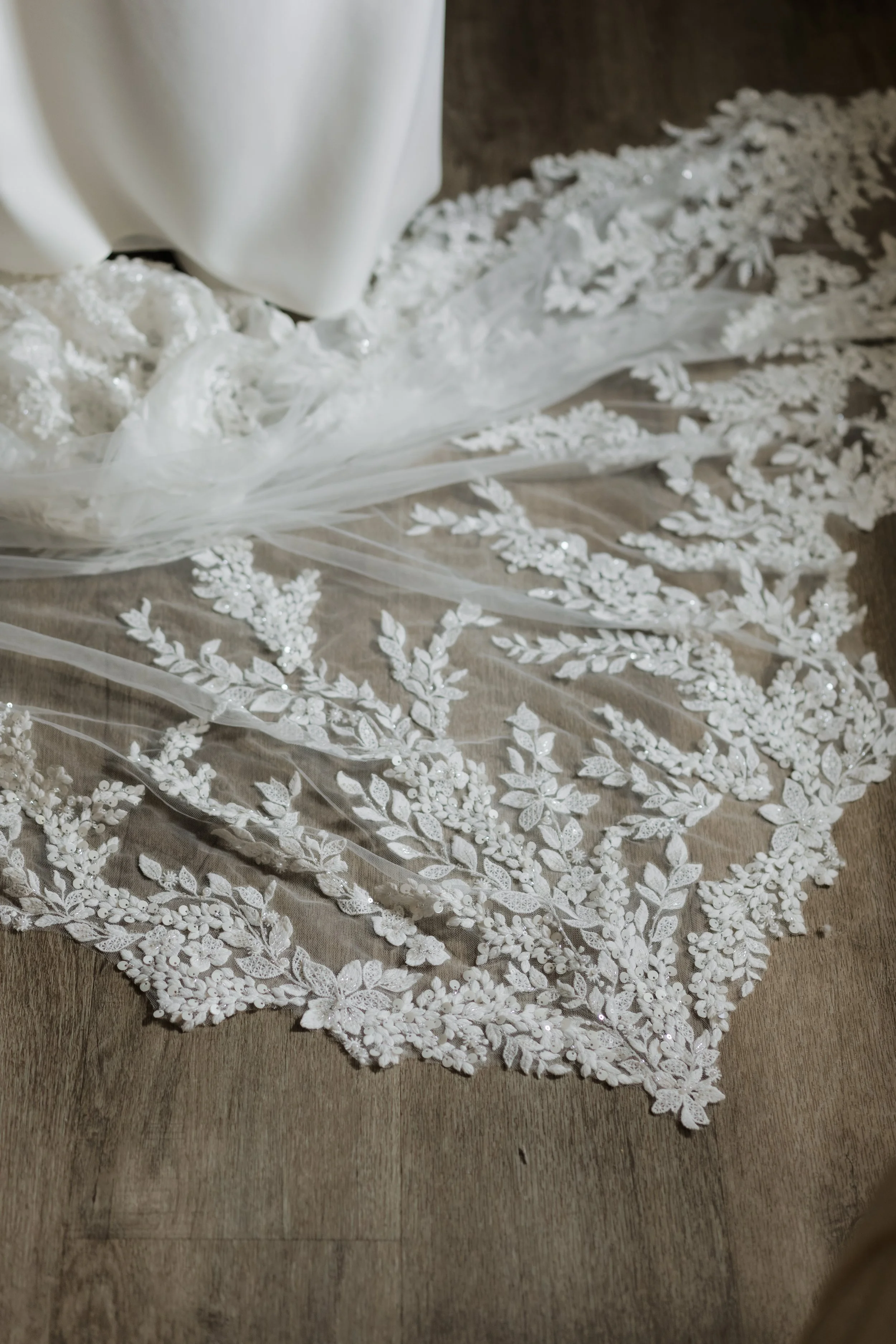 A white bridal veil with intricate floral embroidery lying on a wooden surface.