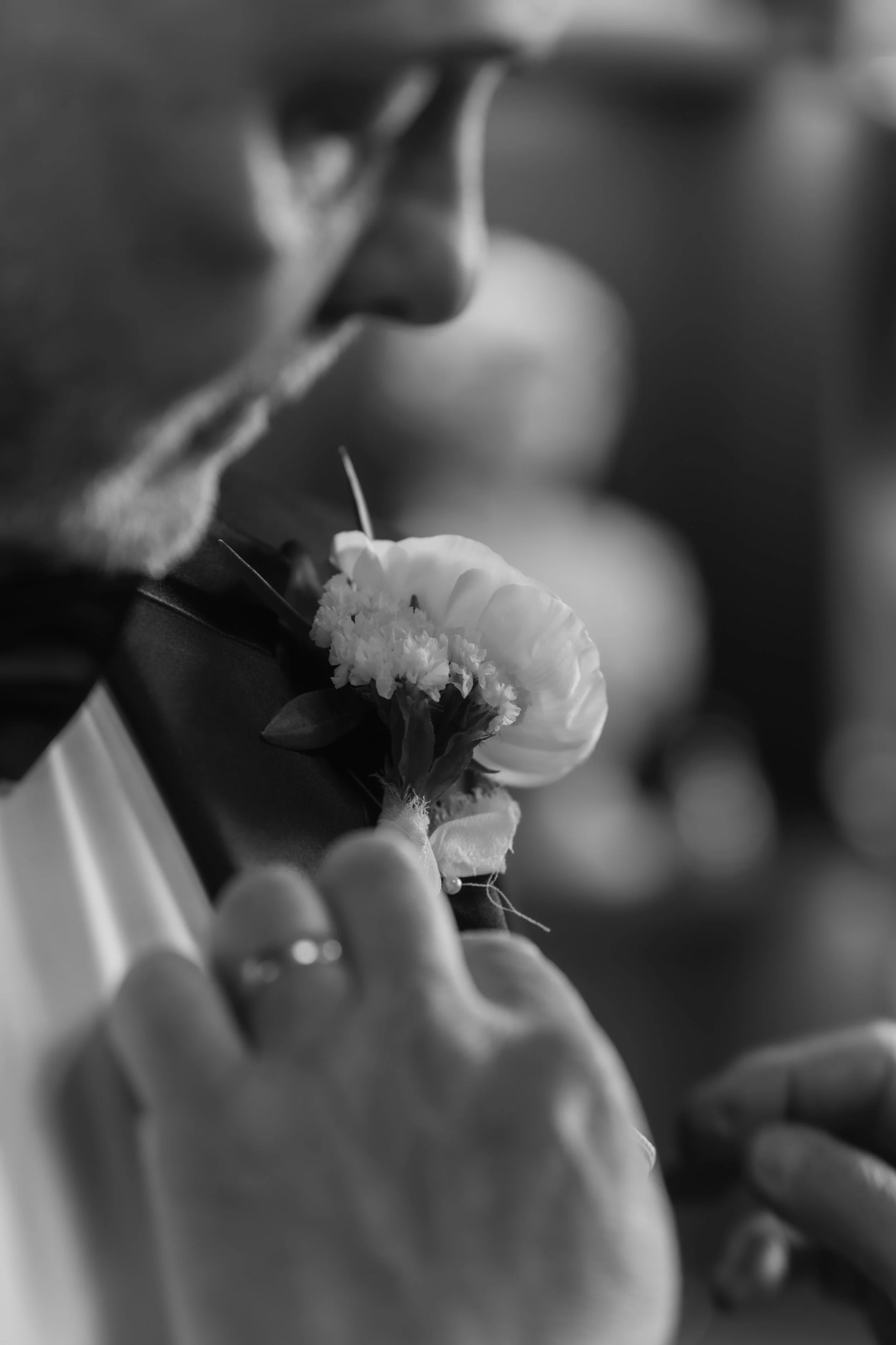 Close-up black and white photo of a man wearing glasses pinning a flower to his lapel