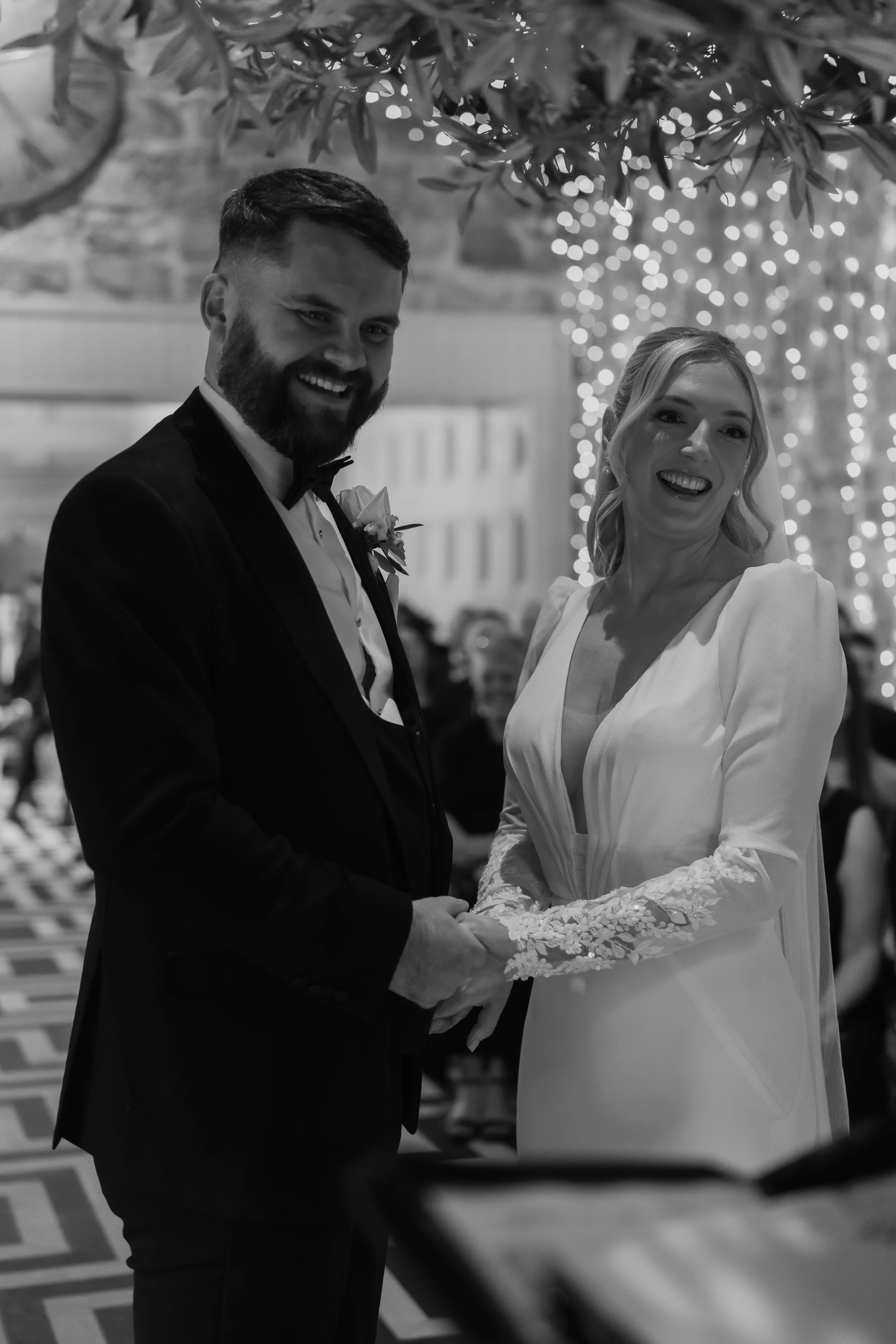 A bride and groom holding hands and smiling at each other during their wedding ceremony.