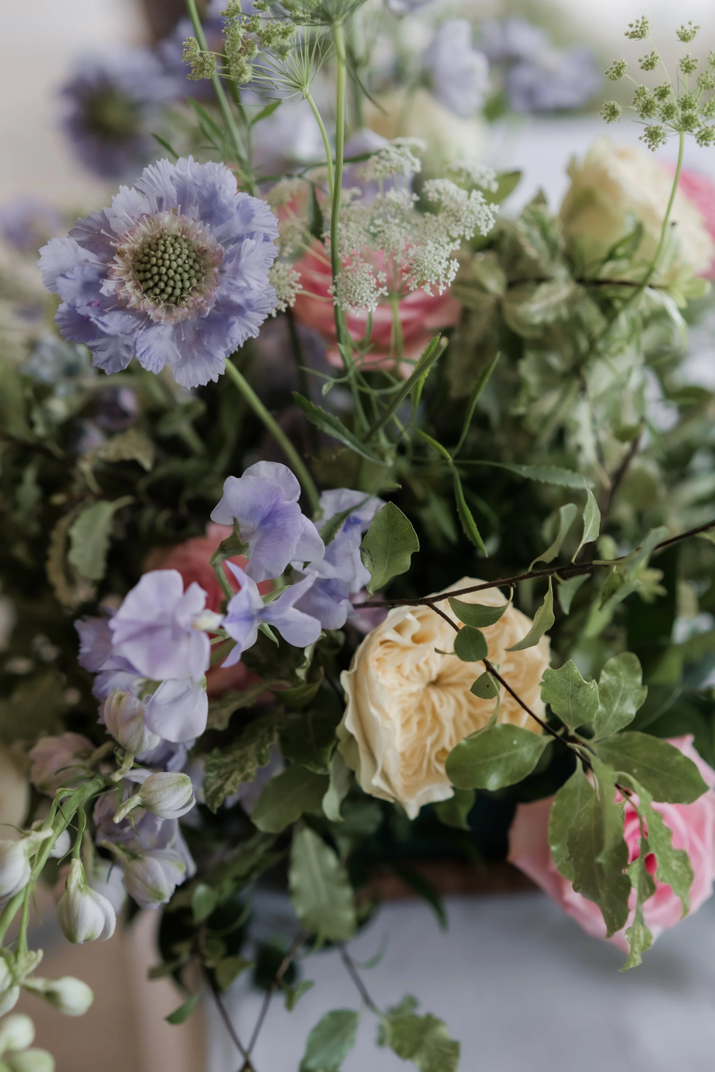 Close-up of a bouquet of light purple, pink, white, and green flowers with greenery.