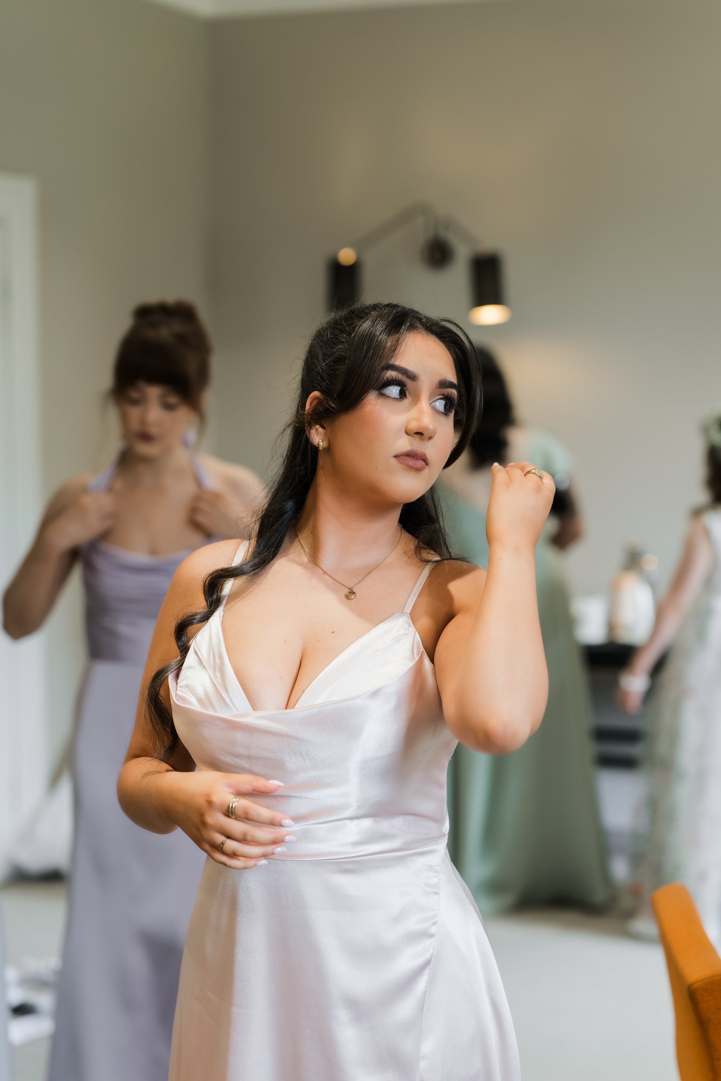 Young woman in wedding dress getting ready with friends in the background.