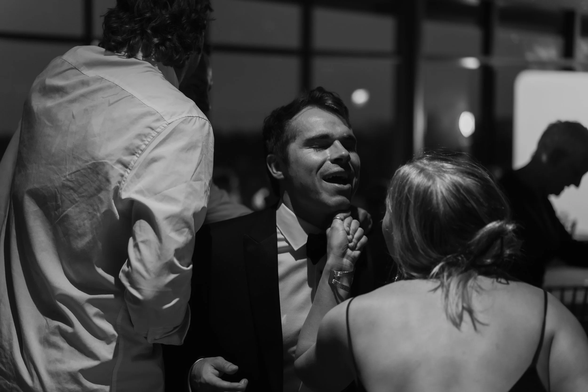 A man in a tuxedo appears distressed as a woman grabs his chin amid a heated argument at a social gathering.