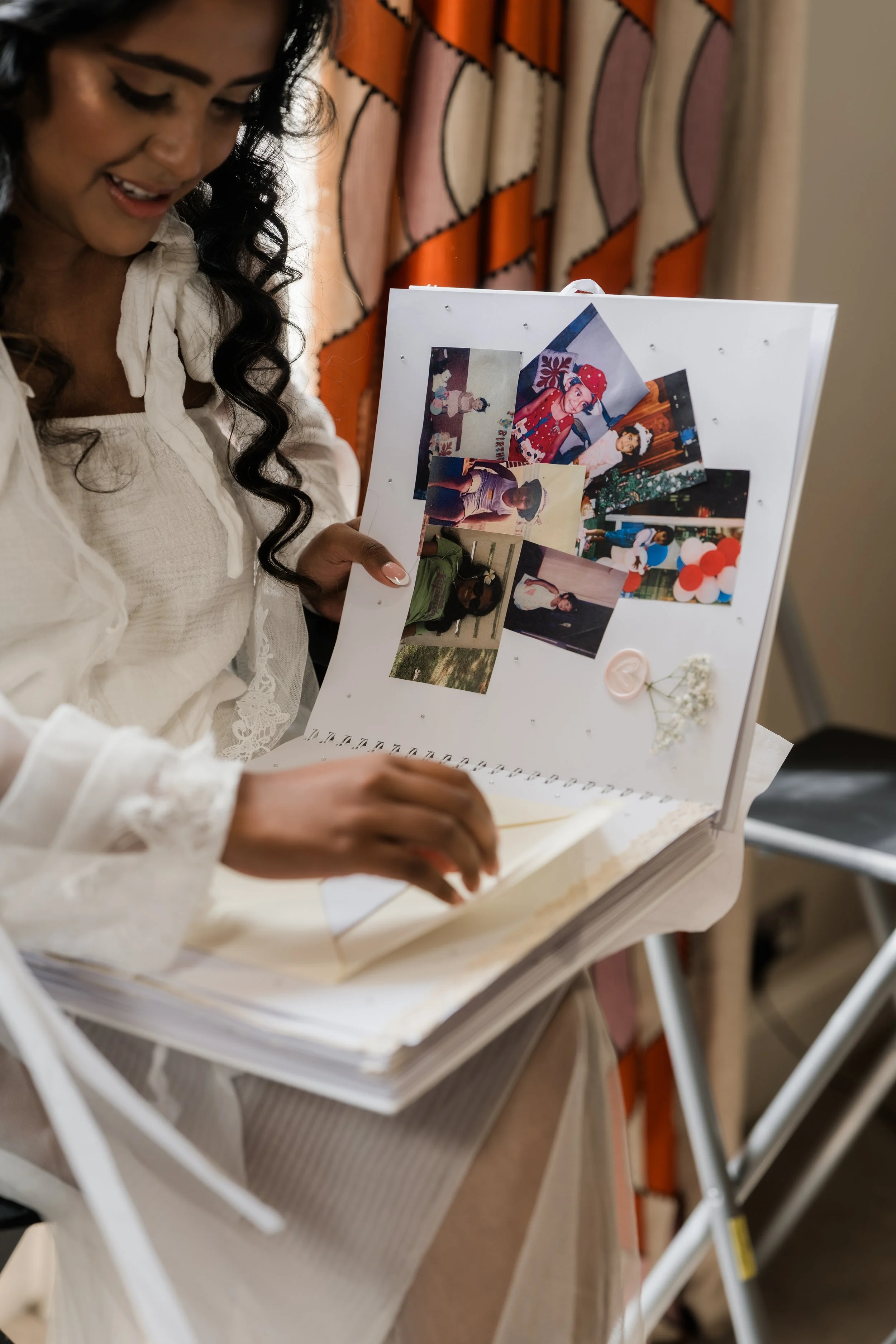 Woman in a white dress looking at a photo album with various photographs and decorative items on the pages.