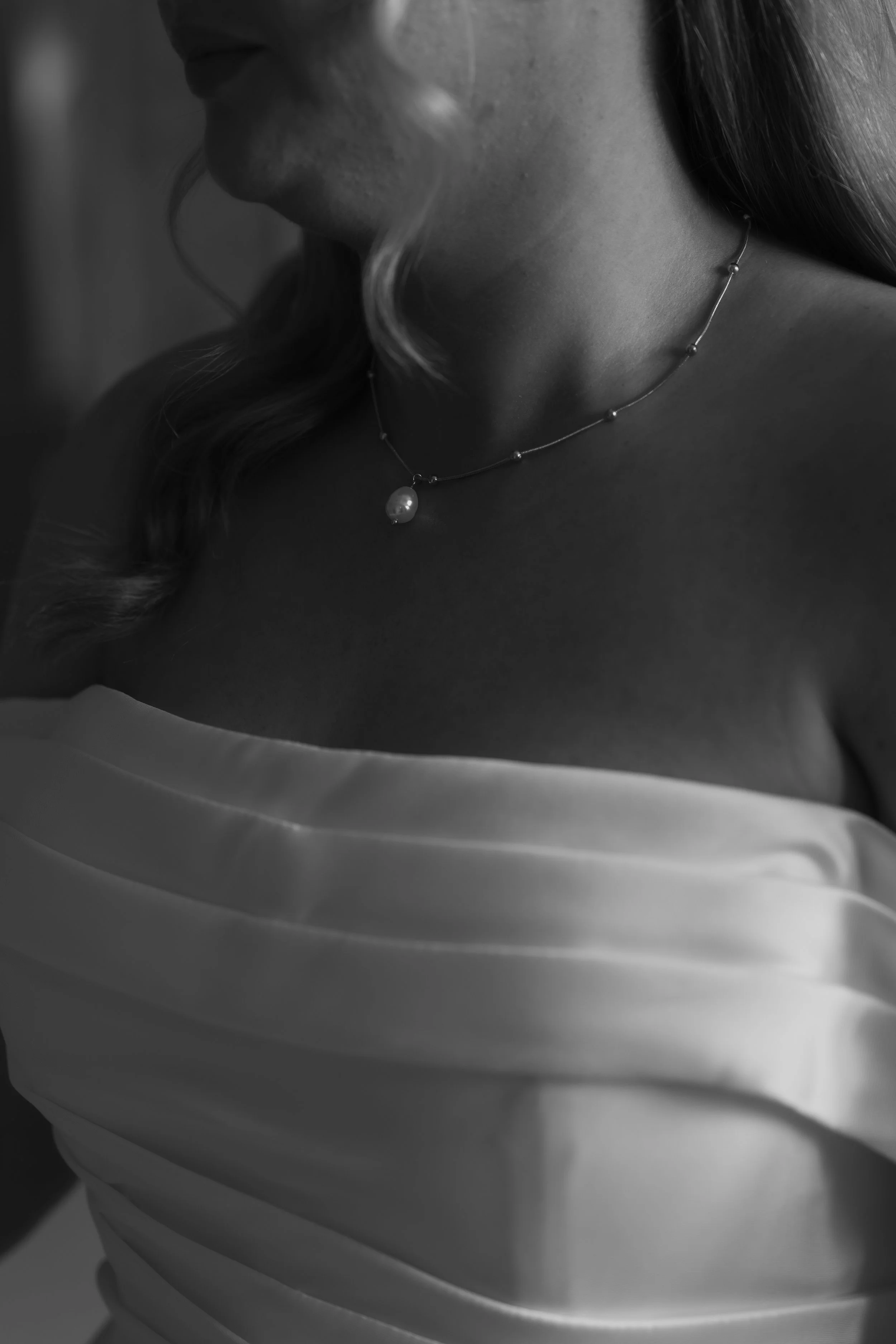 Close-up of a woman wearing a pearl necklace and a strapless satin dress, with wavy hair partially visible.