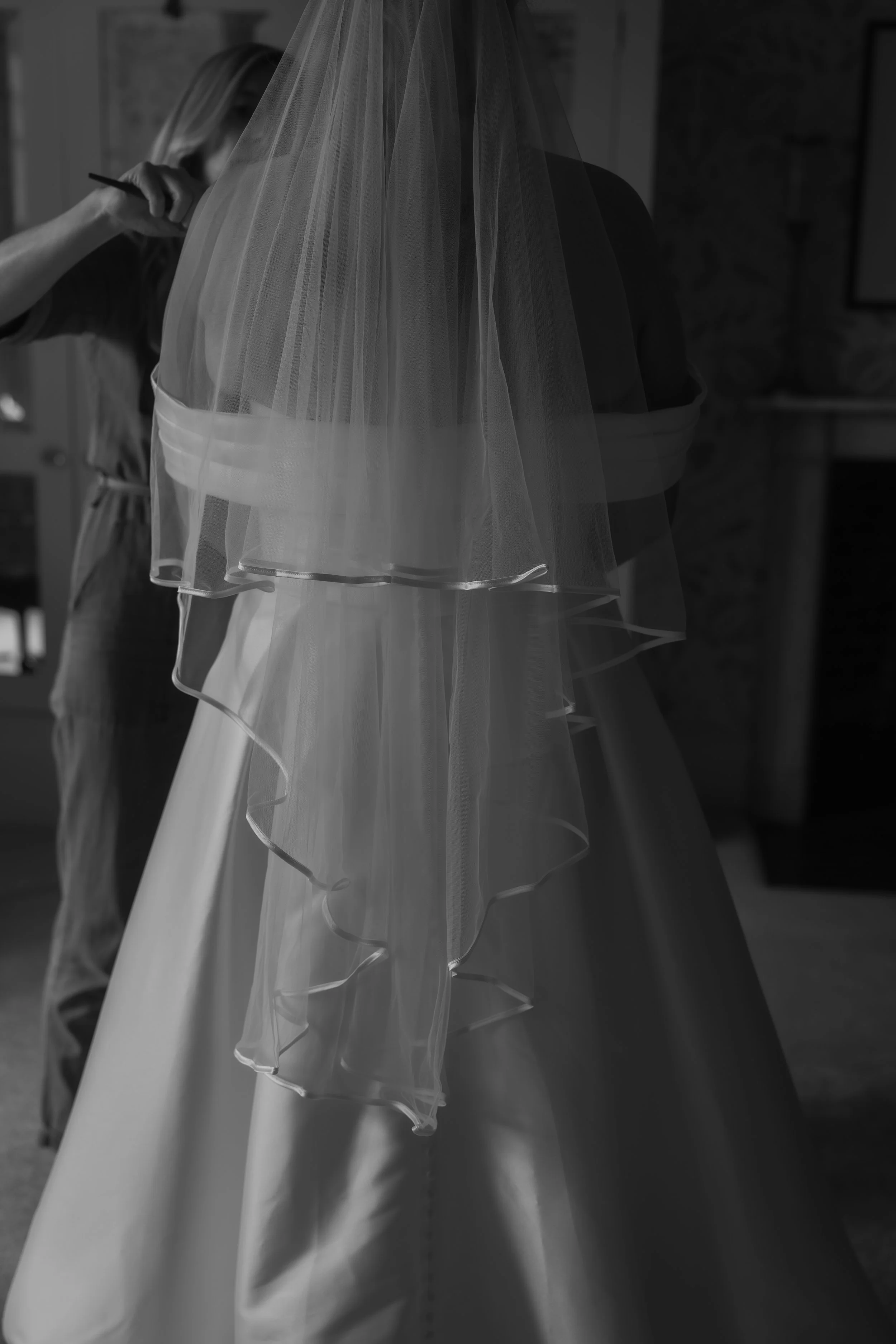 A bride being assisted with her wedding dress and veil by a woman.