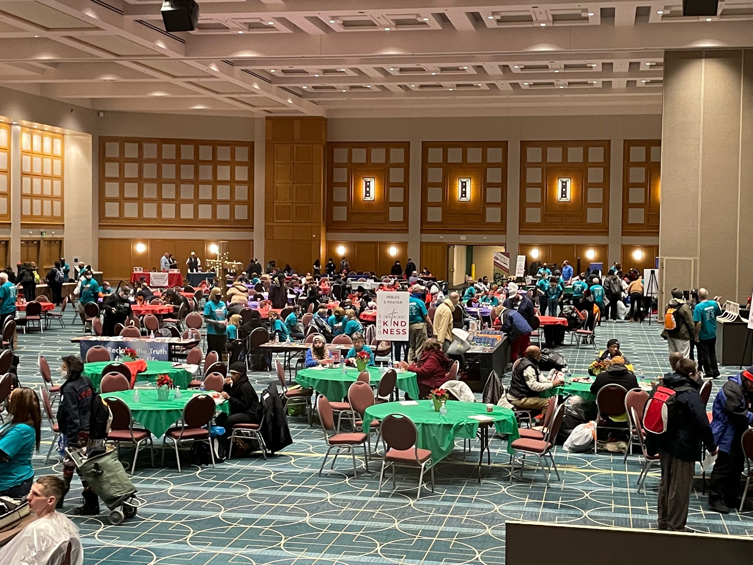 Large indoor event space at the Minneapolis Convention Center filled with people sitting at tables with festive holiday decorations, some standing, and various booths set up in the background.