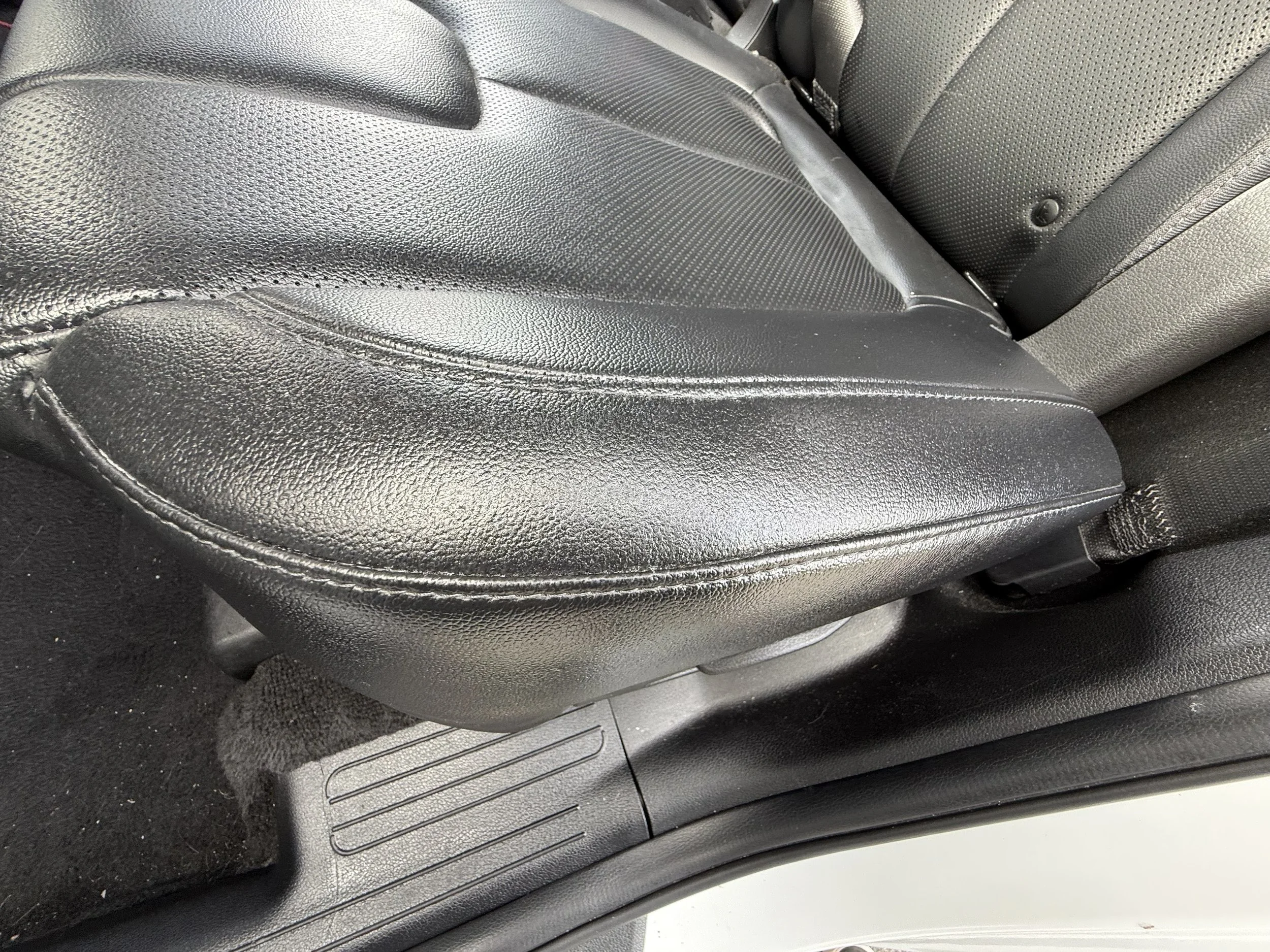 Close-up of a black leather car seat and floor mat with visible stitching and textures.