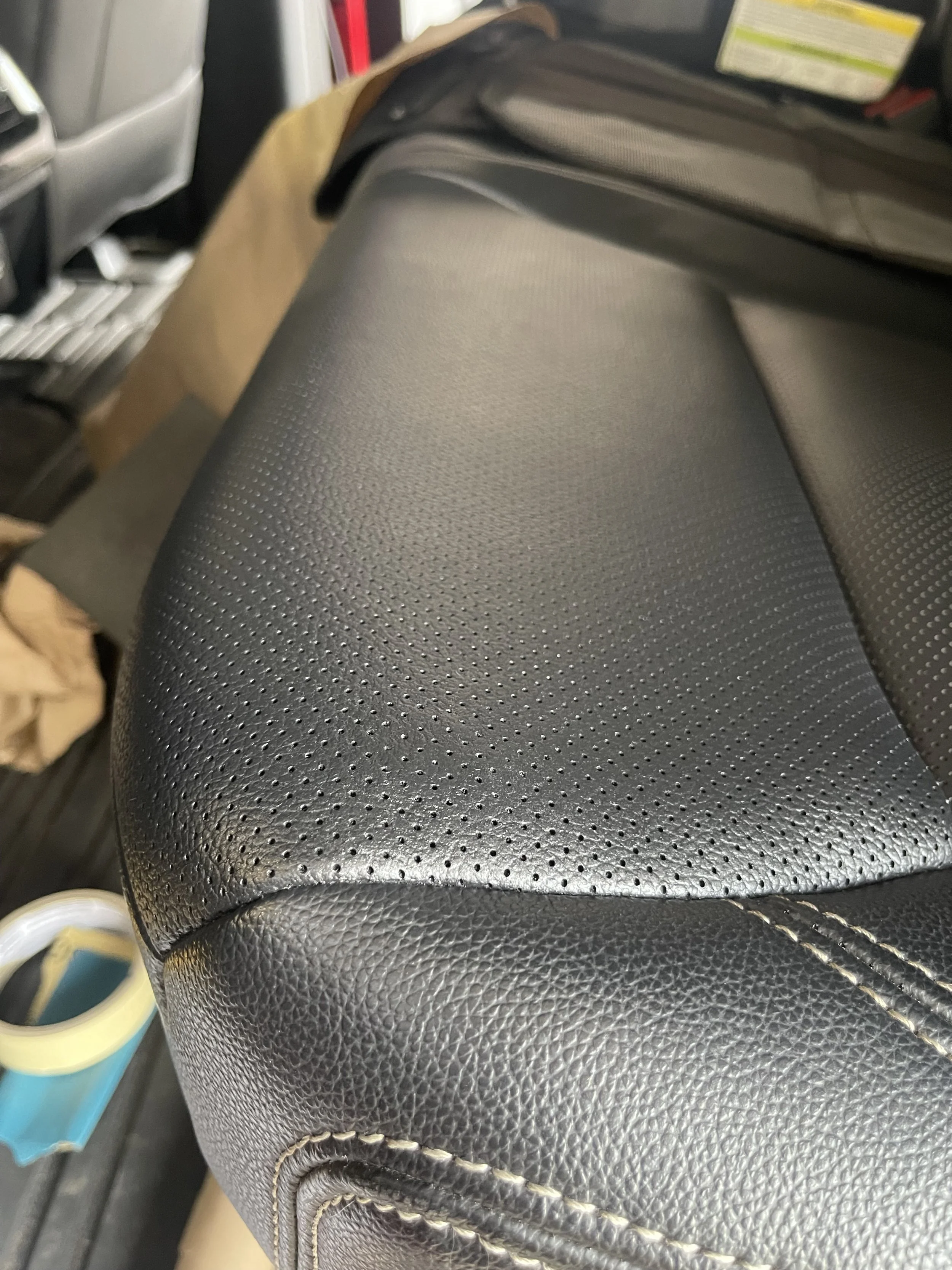 Close-up of a black leather car seat with textured surface and white stitching.