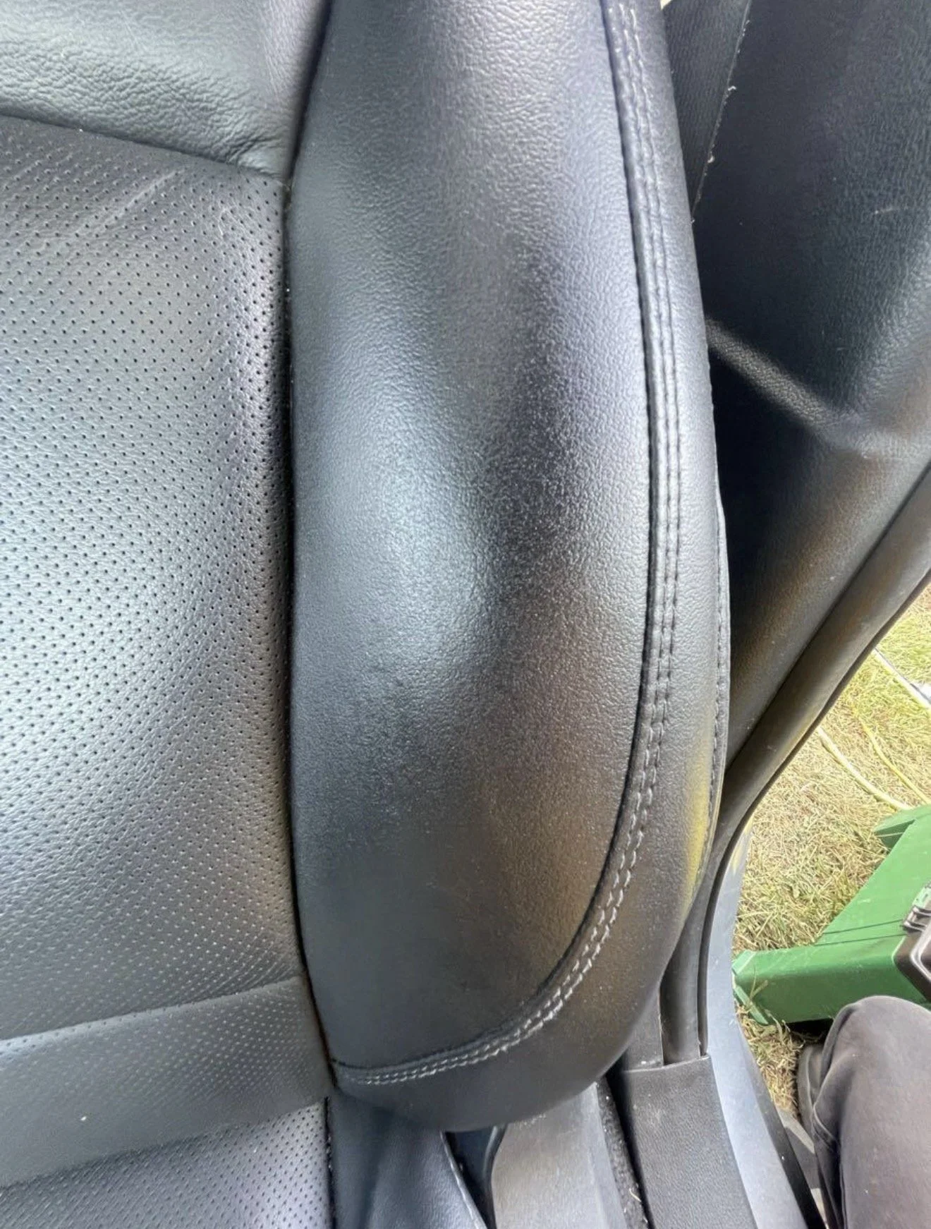 Close-up of a black leather car seat with a headrest and visible stitching.