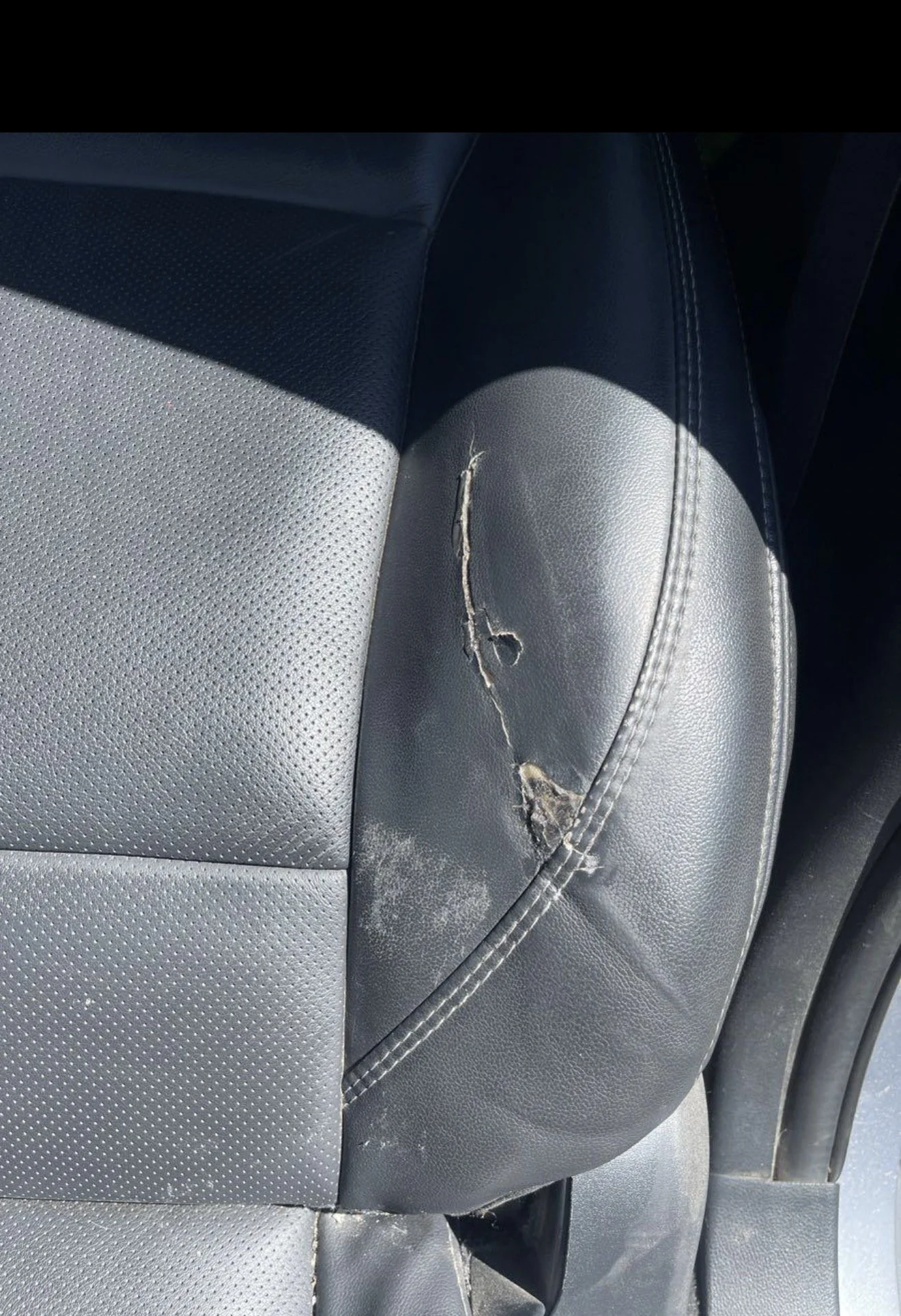 Close-up of a car seat with a large tear and damage to the leather upholstery.