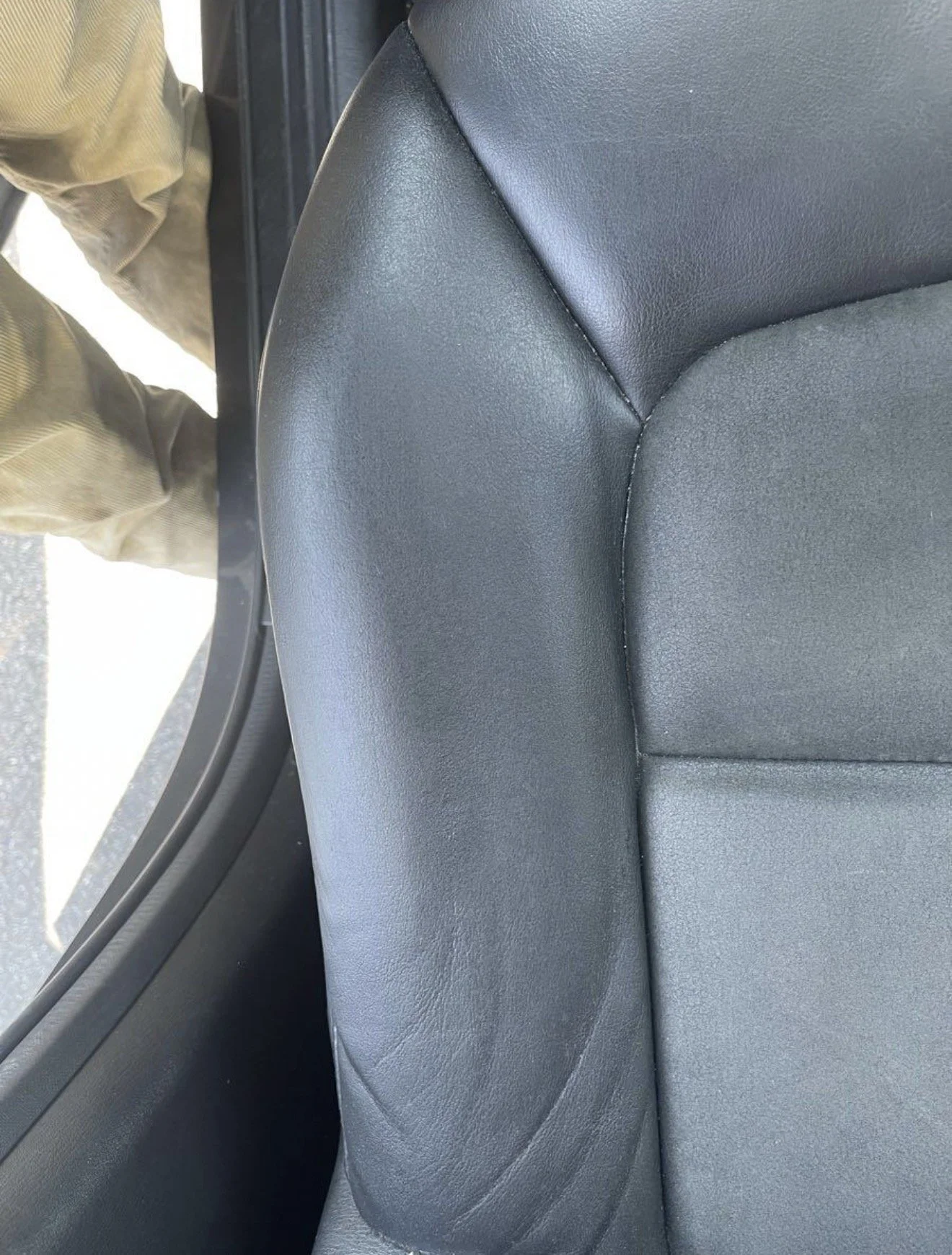 Close-up of a black leather car seat with visible stitching and texture.