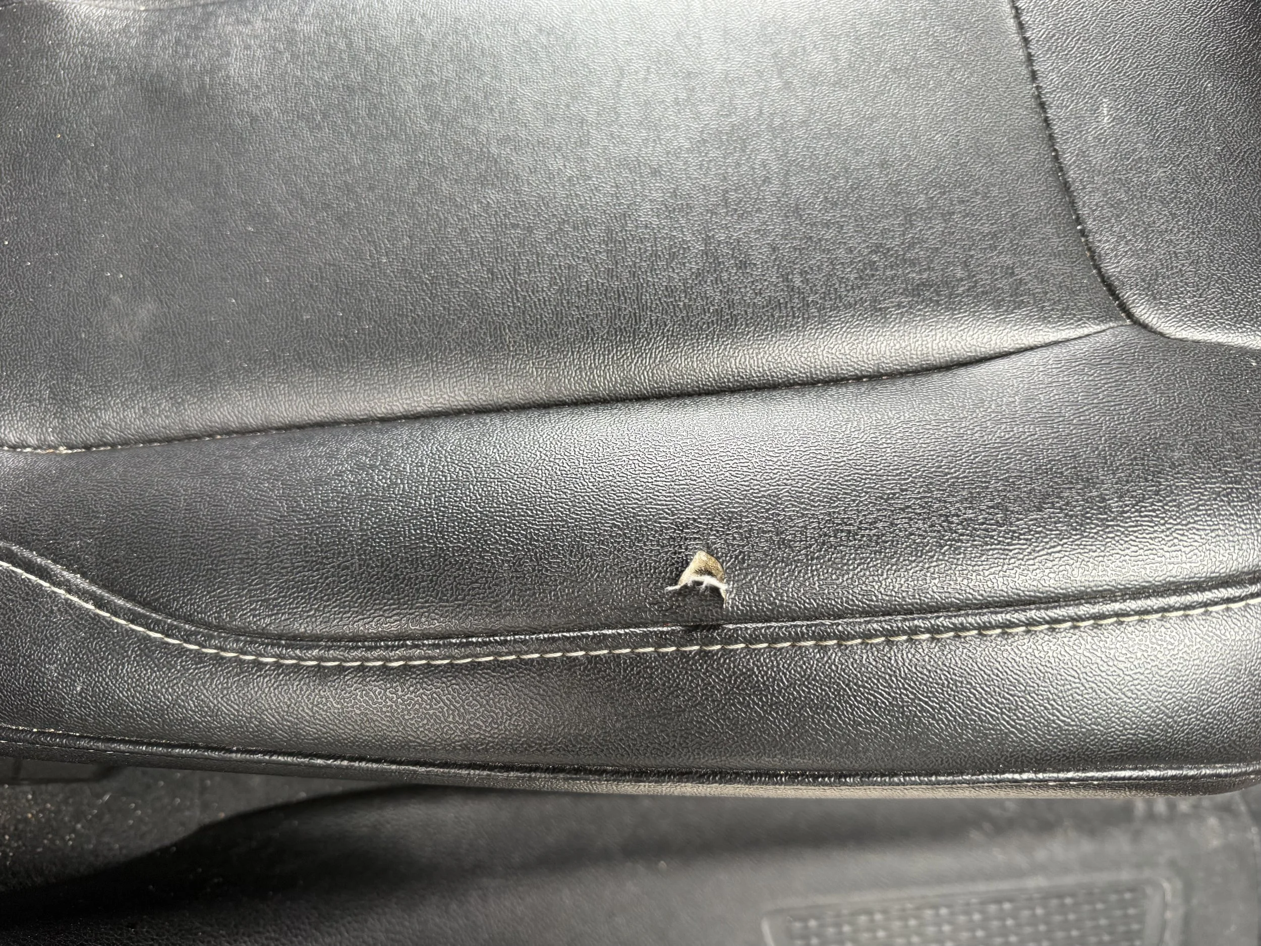 Close-up of black leather car seat with a small tear in the material.