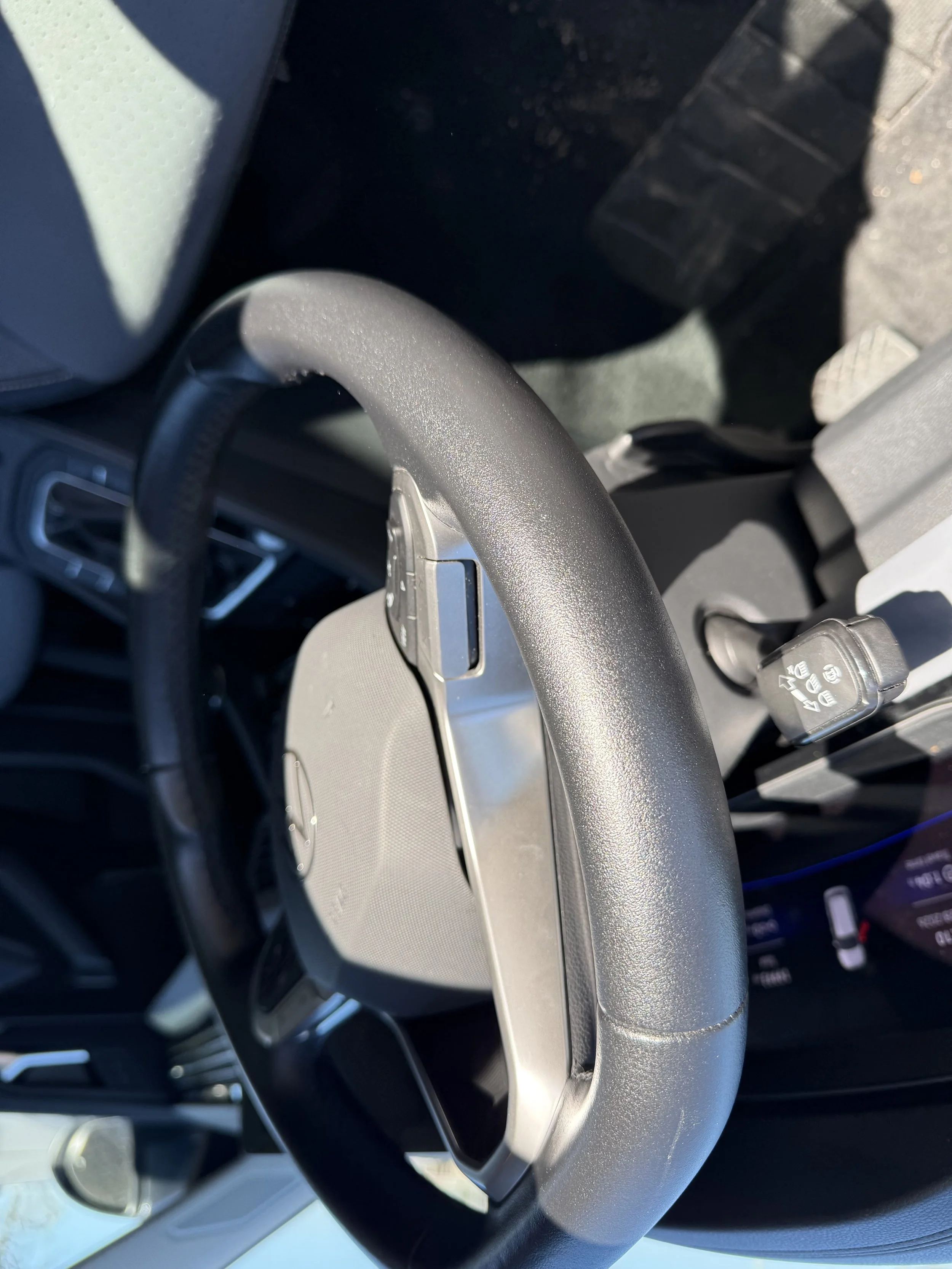 Close-up of a vehicle's steering wheel with a gray dashboard and controls visible.