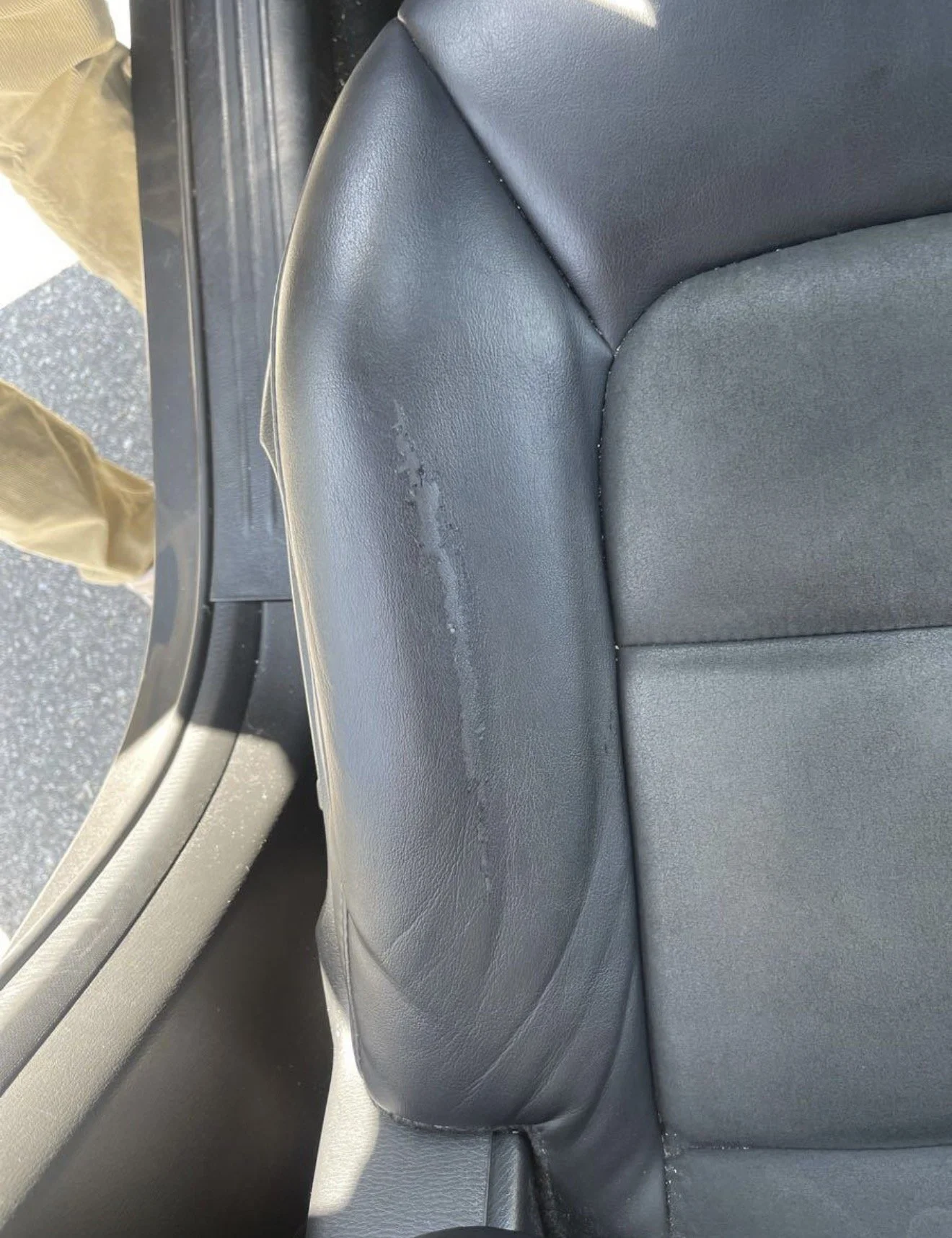 The back seat of a car with black leather upholstery, showing a scratch or scuff on the armrest.