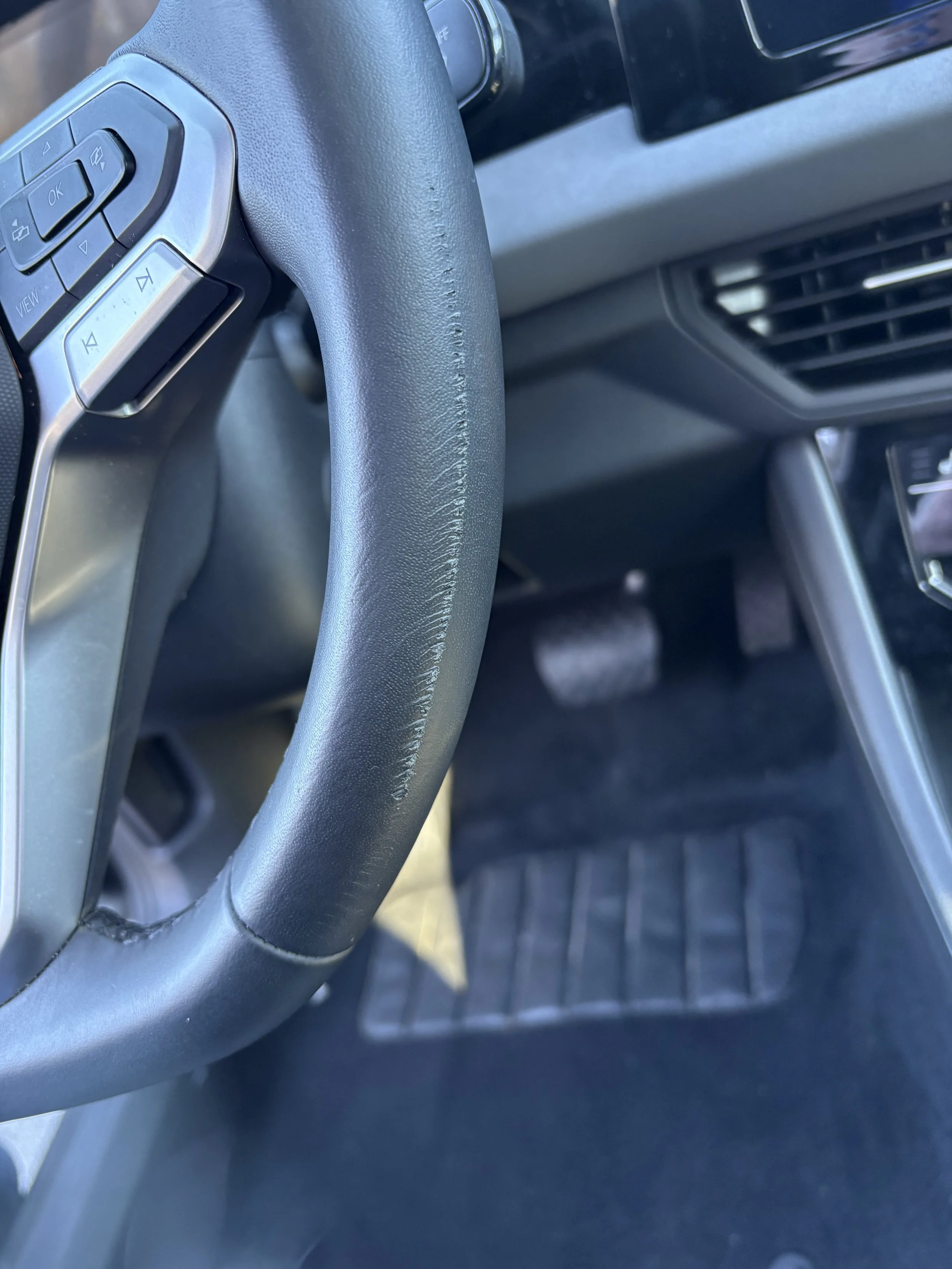 Close-up of a car's steering wheel and driver's side floor mat.