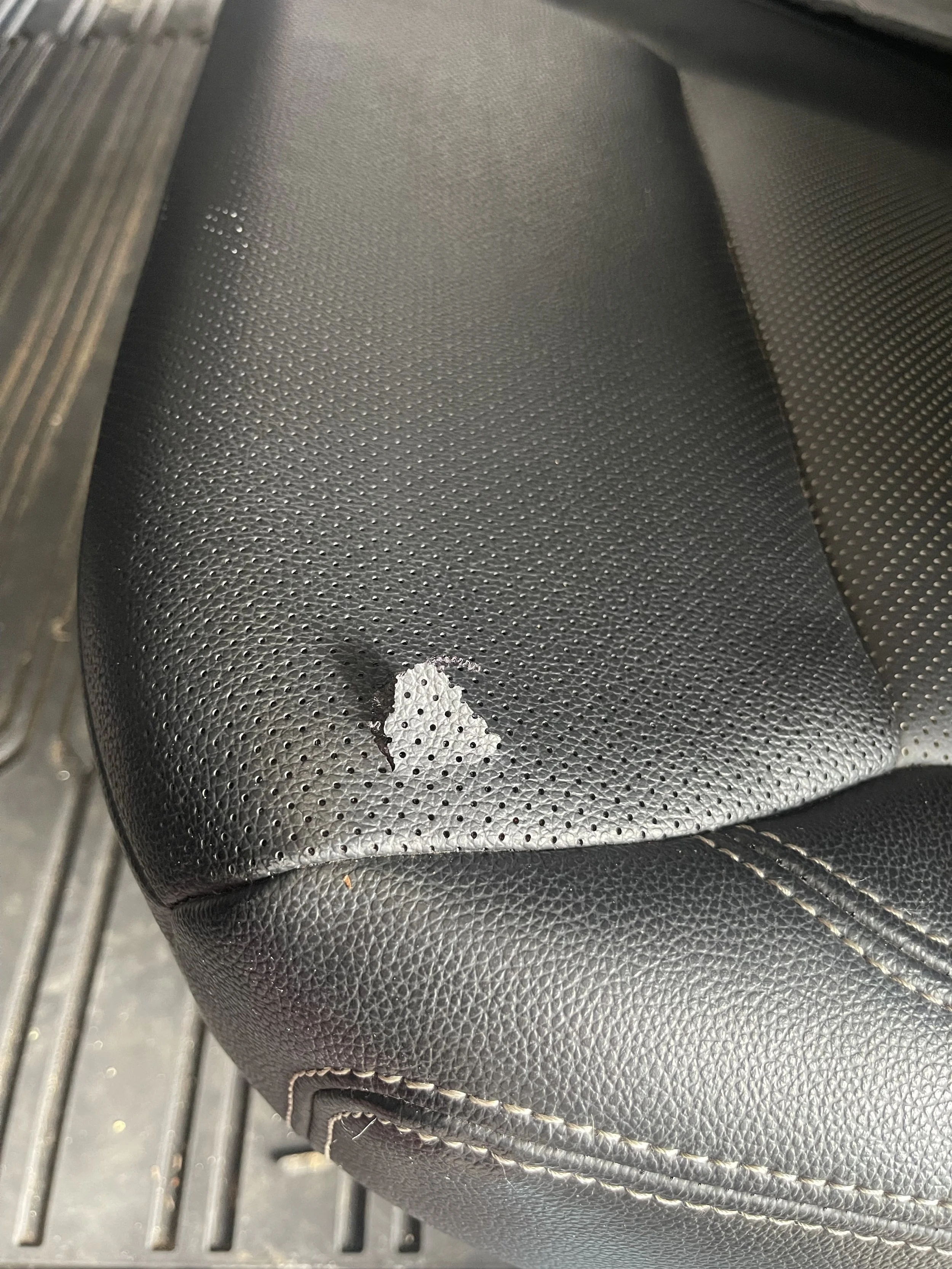 Close-up of a black, textured leather car seat with peeling near the edge.