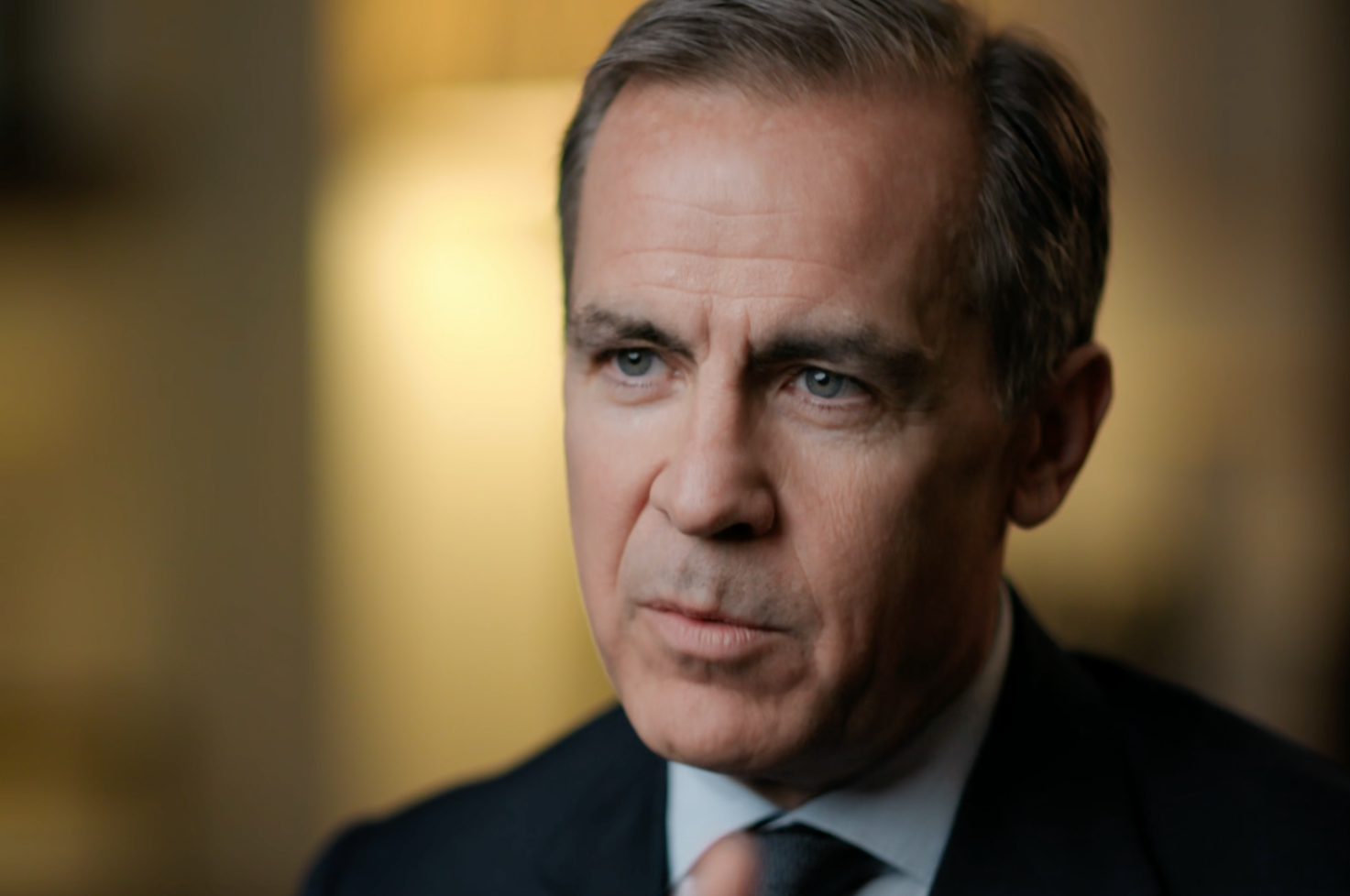 Close-up of a middle-aged man in a suit with brown hair and blue eyes, looking serious and contemplative.
