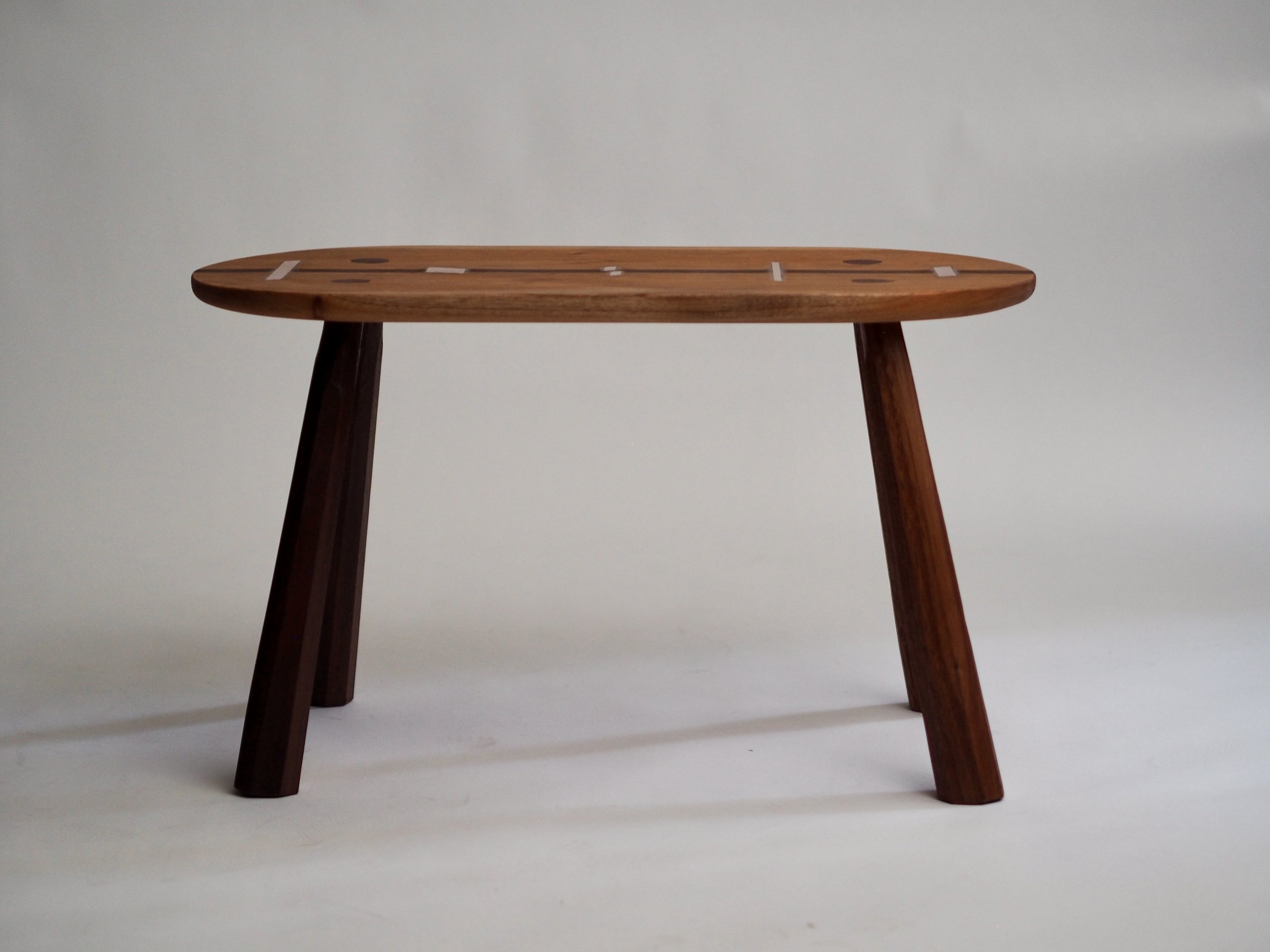 pill-shaped mahogany bench table with tapered faceted legs and copper inlay