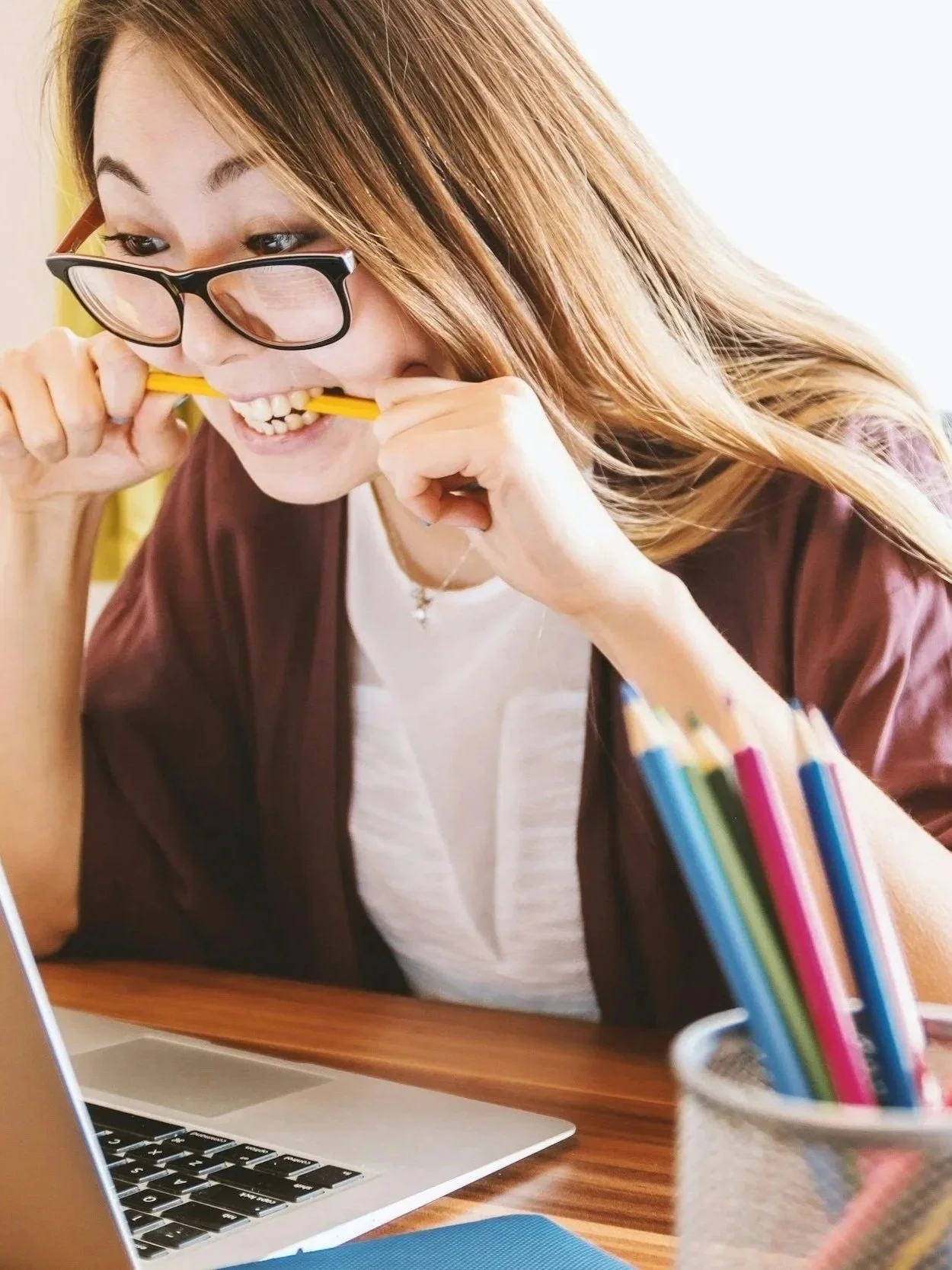 Stressed out Asian woman biting her pencil looking at her laptop