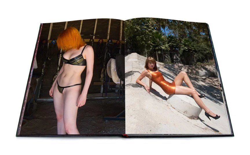 The left spread shows a photo of a woman with red hair wearing an olive latex bikini. Her face is covered by her hair. The right spread shows a woman with light brown hair wearing an orange latex dress and heels sitting at an angle on concrete.