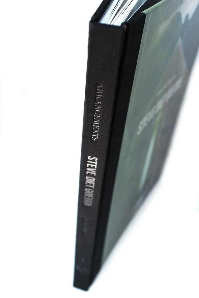 The fabric spine shows the embossed text. The visible text reads "Arrangements Steve Diet Goedde"  The photos focus fades as it goes further down.