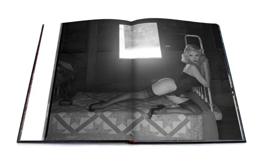 This open spread shows a black and white photograph of a blonde woman in lingerie and heels on a vintage steel frame bed leaning across the bed holding onto the frame.