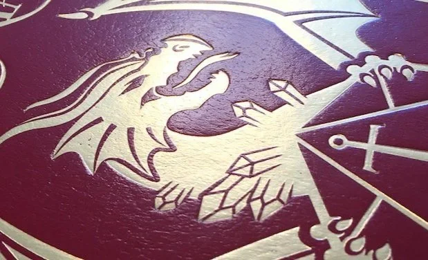 Close-up of the deluxe cover for Critical Role: The Chronicles of Exandria Vol. I: The Tale of Vox Machina, showing the gold foil dragon’s horned head, open mouth, wings, and claws around the Critical Role logo