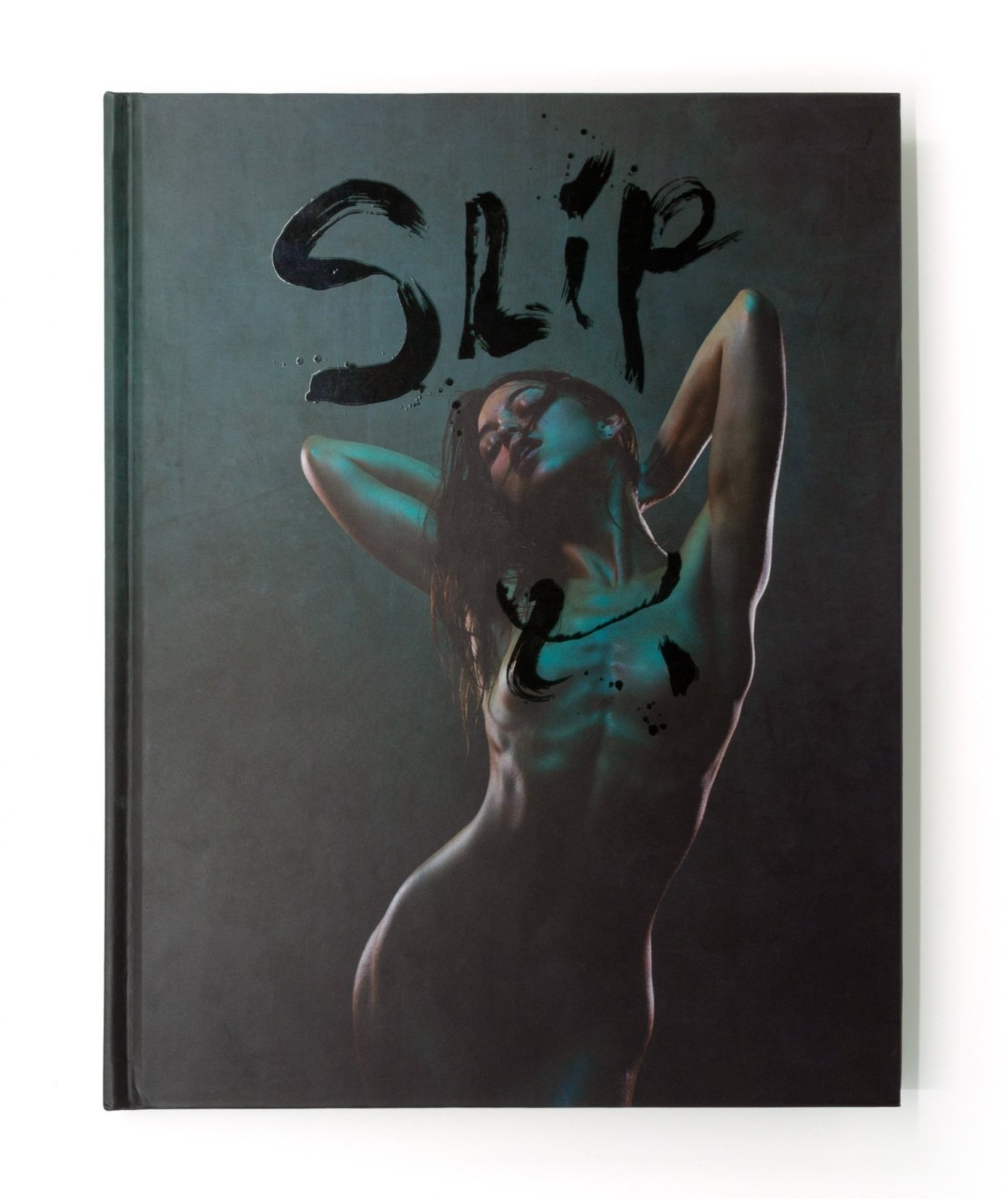 The text of this book cover reads "SLIP" in brush lettering. The cover art is a photograph of a petite nude woman with brown hair. Her arms are reaching behind her. The background is teal and teal shadows reflect on the woman.