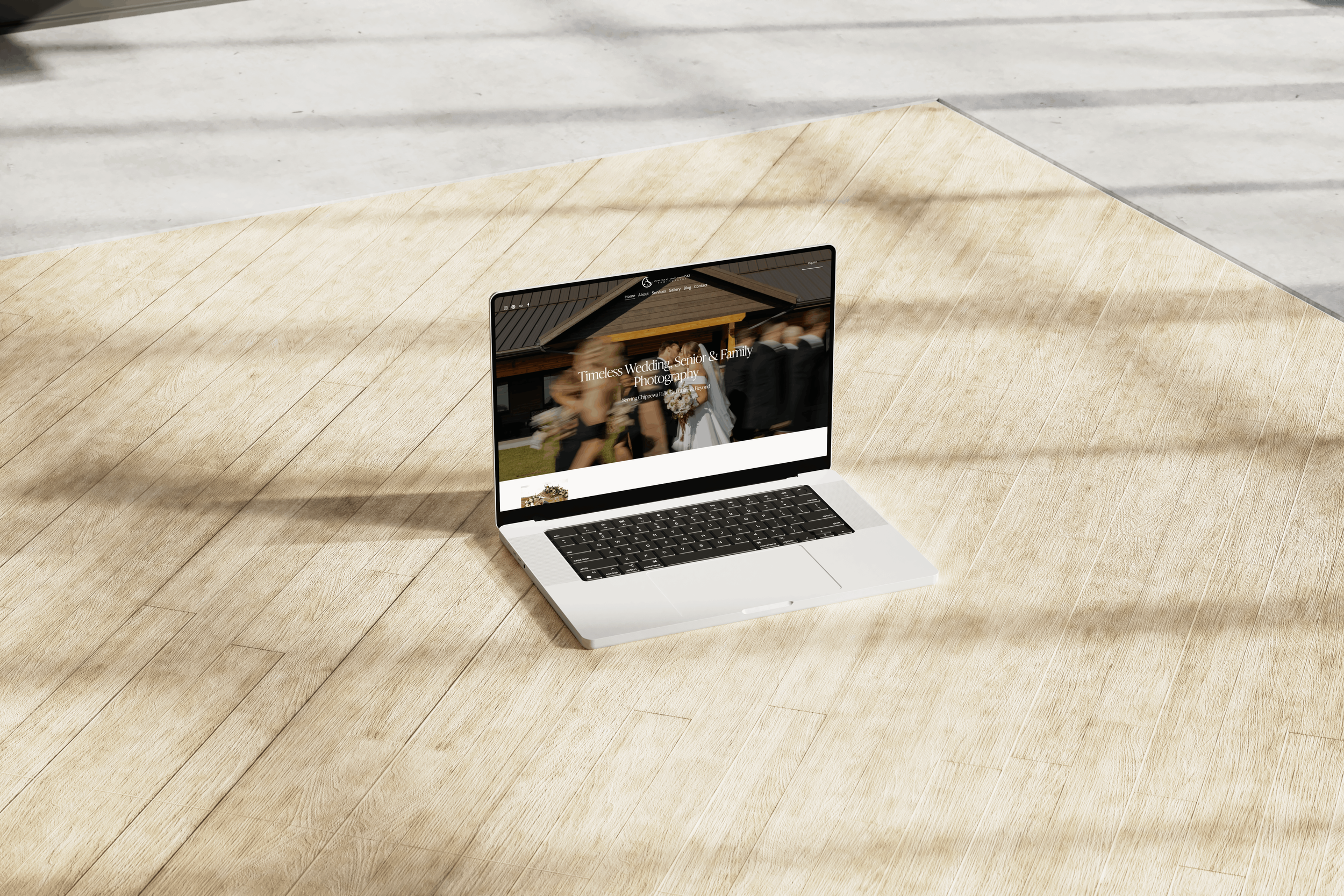 A laptop on a wooden floor displaying a wedding photography website