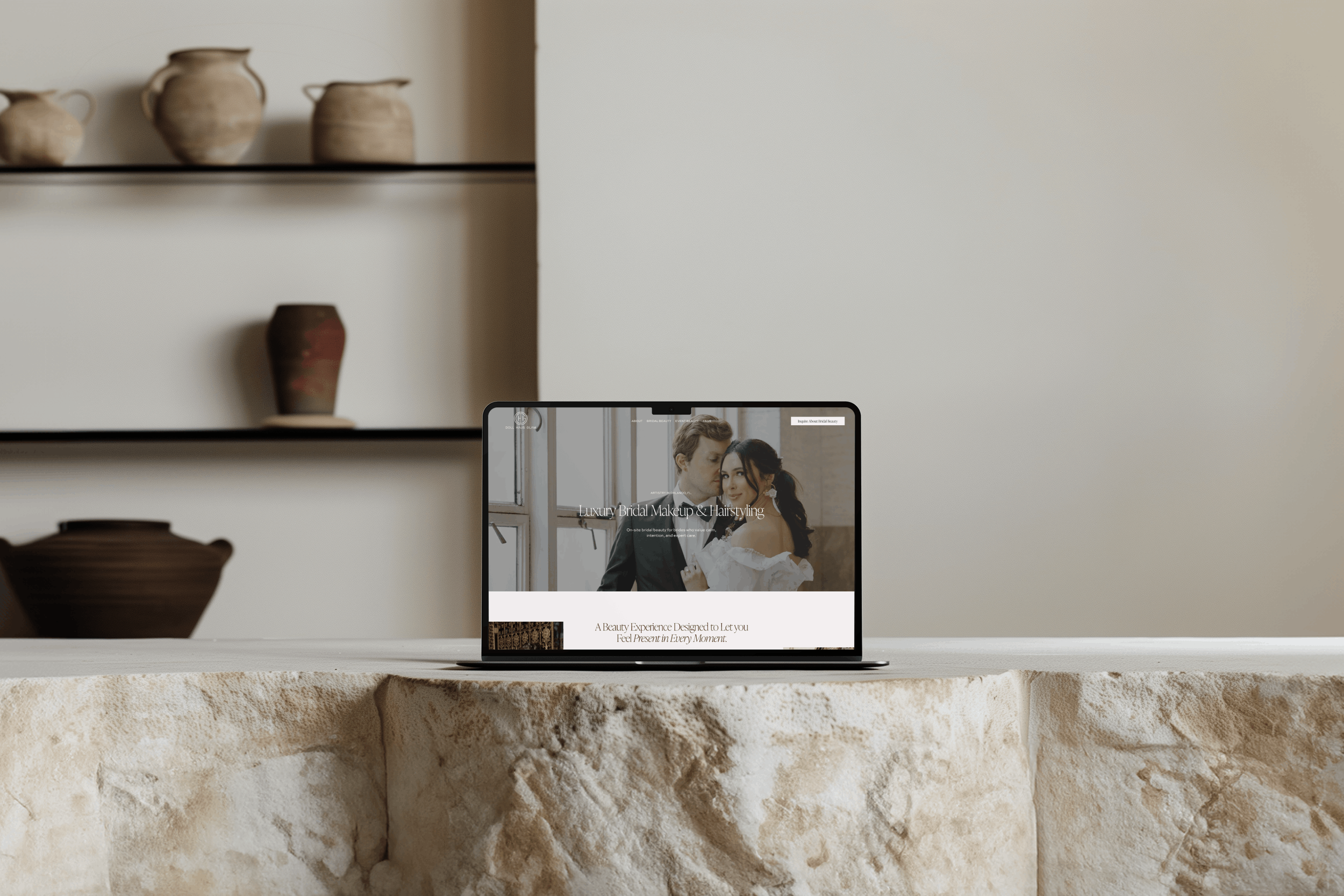 Laptop on a stone surface displaying a bridal makeup and hairstyling webpage with a bride and groom in the background.