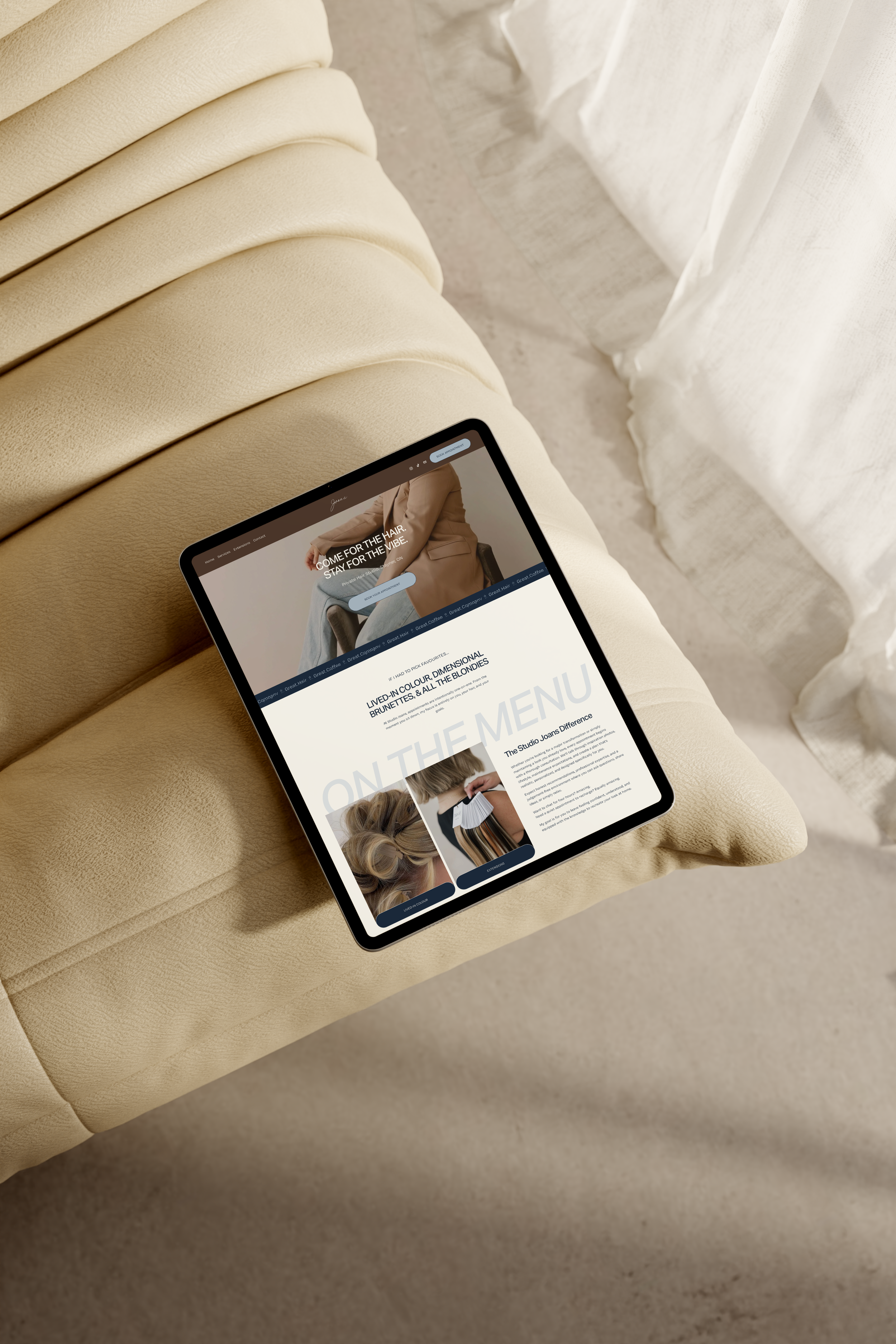A tablet on a beige leather sofa displaying a website about hair styling services, with images of models with different hair styles.