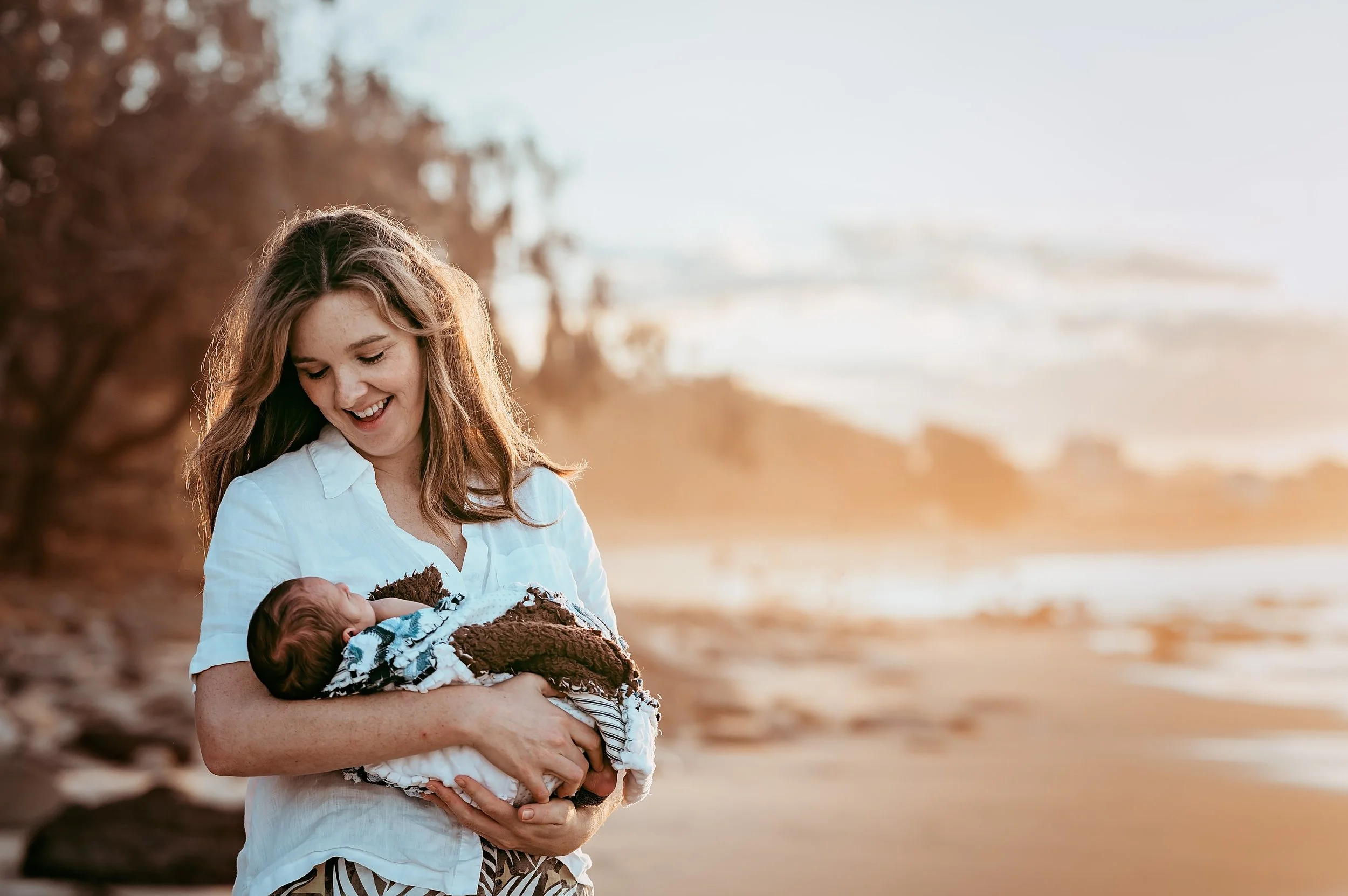 A woman looking lovingly at her new born baby on a beach setting