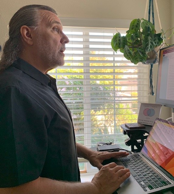 Therapist working at a desk with plants nearby, representing a grounded, supportive online therapy setting.