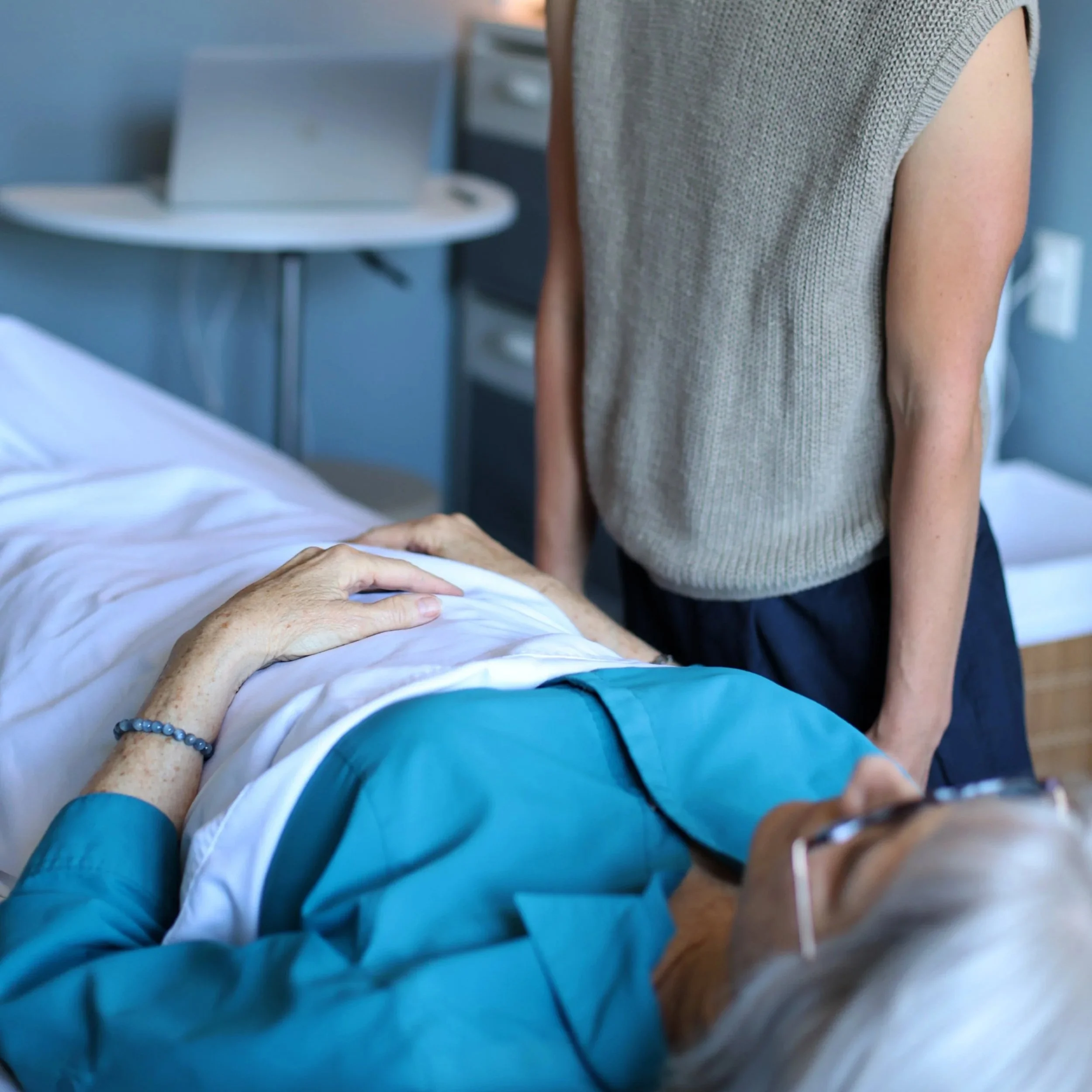 A woman performs a medical procedure on a patient lying on a hospital bed in a clinic room.