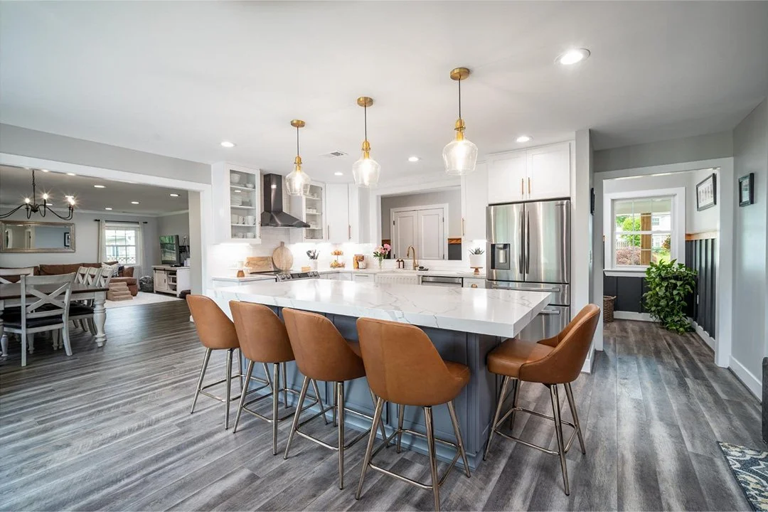 A luxury kitchen with a white quartz island, brown chairs around the island, and gold pendant lights.