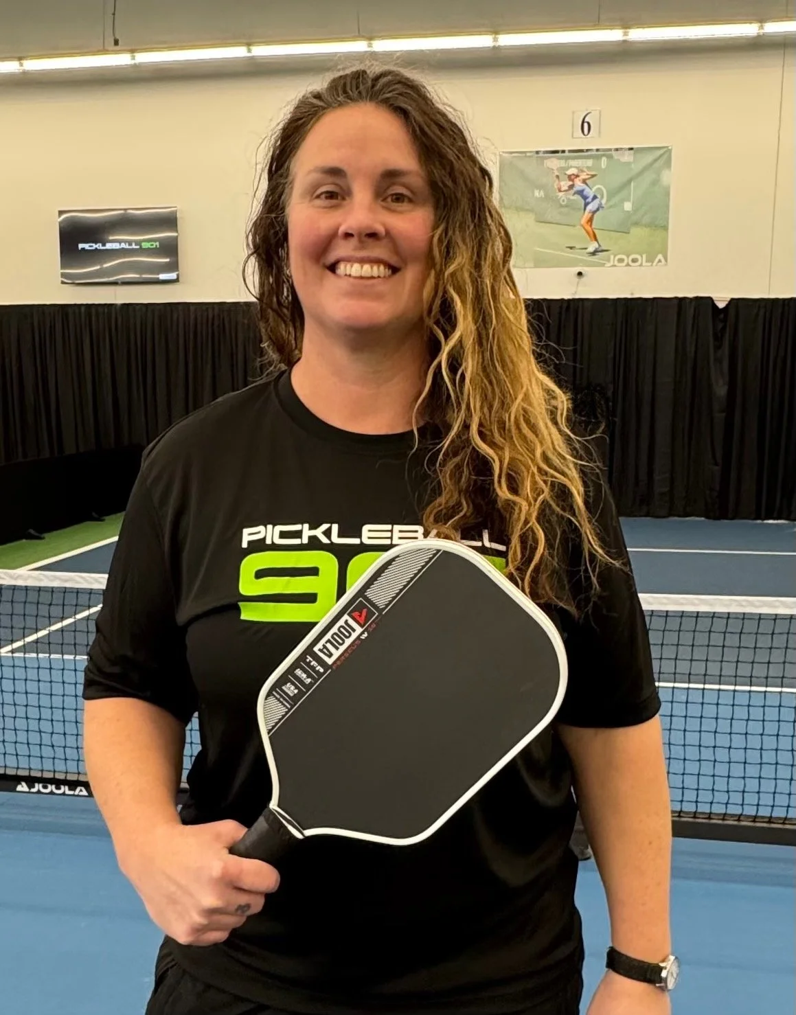 Person holding a pickleball paddle on a court in a blue shirt.