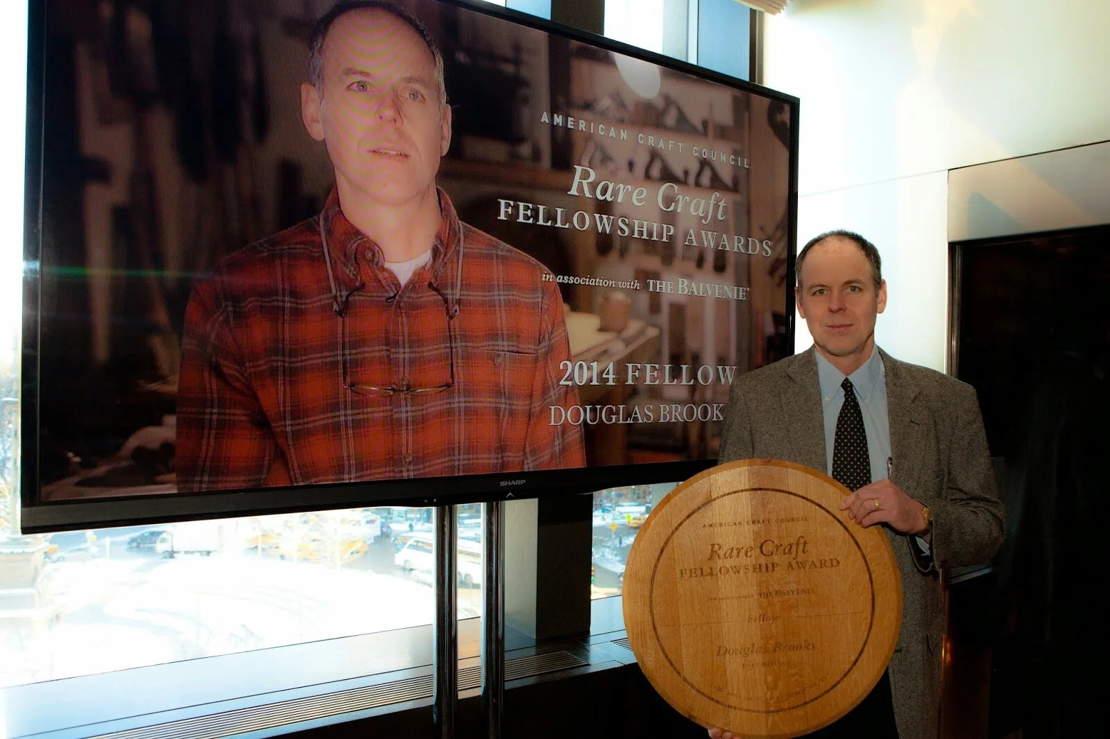 Douglas Brooks holding the 2014 Rare Craft Fellowship Award wooden plaque from the American Craft Council.