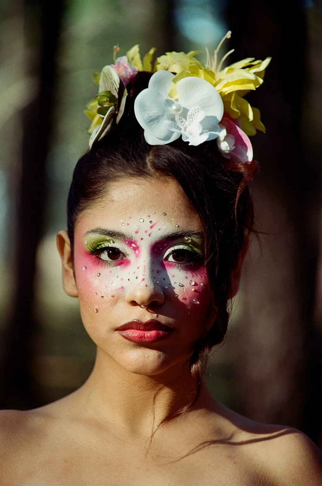 A woman with elaborate makeup, rhinestones on her face, and a floral headdress with orchids and other flowers.