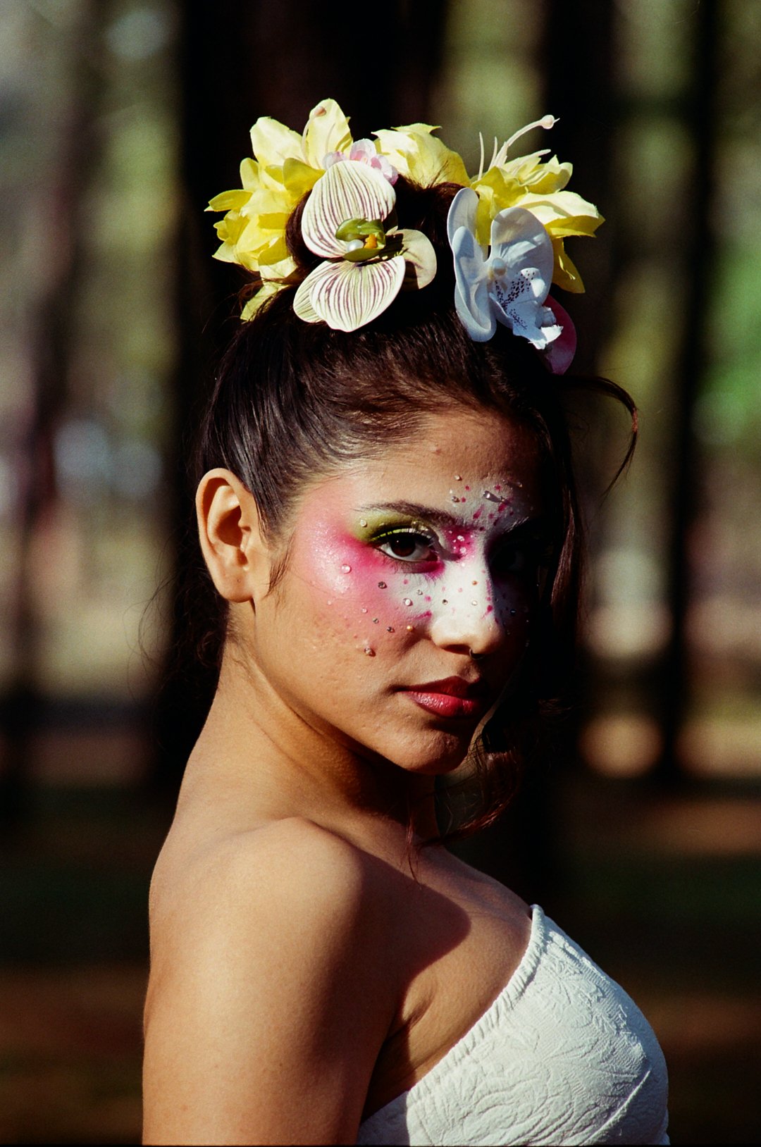 A woman with elaborate makeup and a floral headpiece in an outdoor setting.