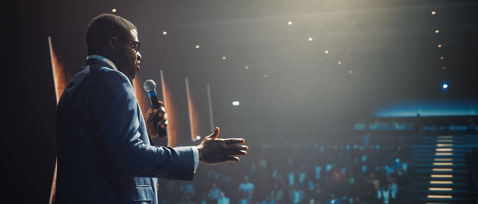 Corporate event presenter holding a wireless microphone with audience, event audio production support