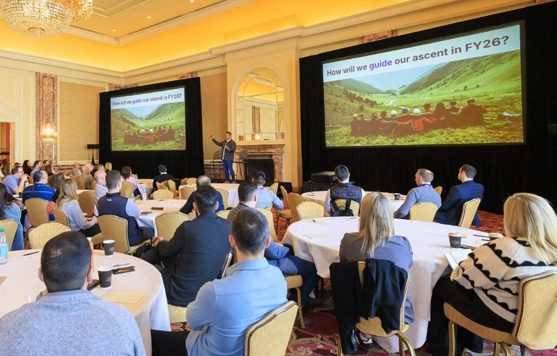 Large breakout session with projection screens, audience seating, and presenter on stage