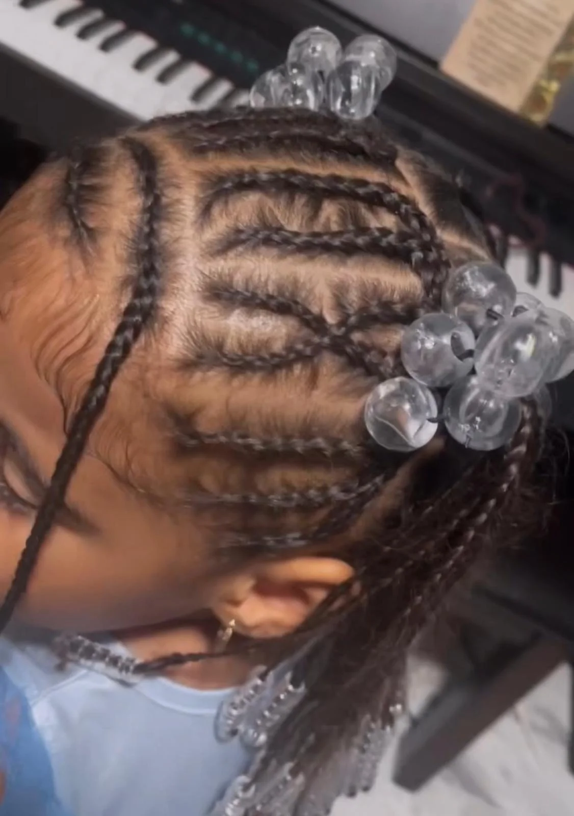 Close-up of a person's head with black braids secured with large clear hair clips and beads, with a keyboard in the background.